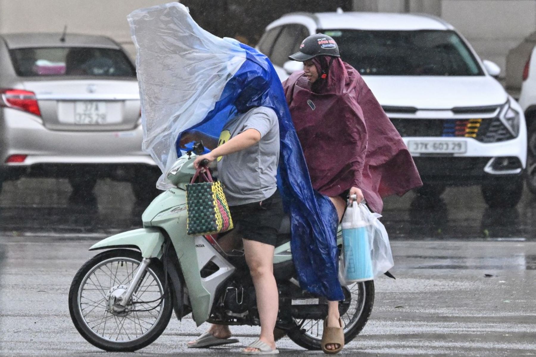 Personas con impermeables se protegen de los fuertes vientos mientras conducen una motocicleta en la ciudad de Vinh, provincia de Nghe An, en Vietnam, el 25 de agosto de 2025, tras la llegada del tifón Kajiki. Foto: AFP