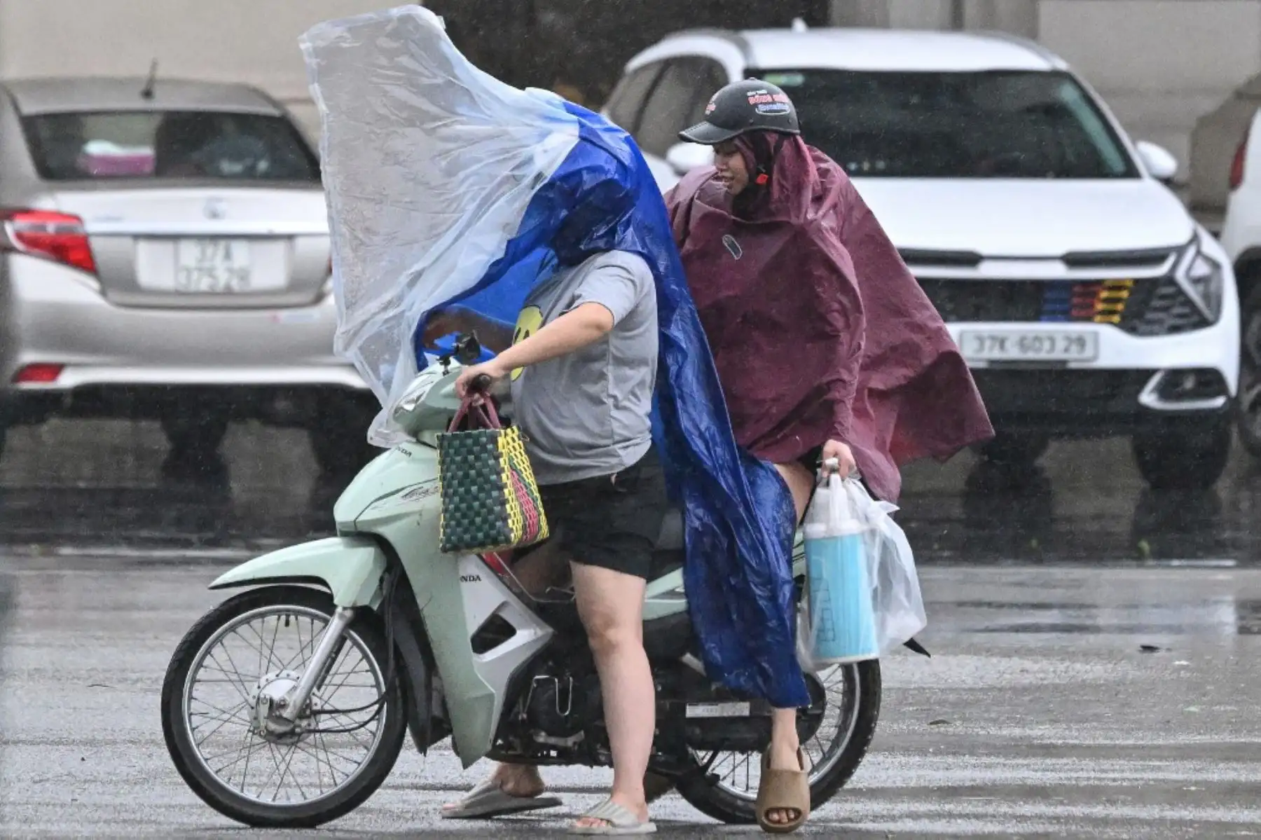 Personas con impermeables se protegen de los fuertes vientos mientras conducen una motocicleta en la ciudad de Vinh, provincia de Nghe An, en Vietnam, el 25 de agosto de 2025, tras la llegada del tifón Kajiki. Foto: AFP
