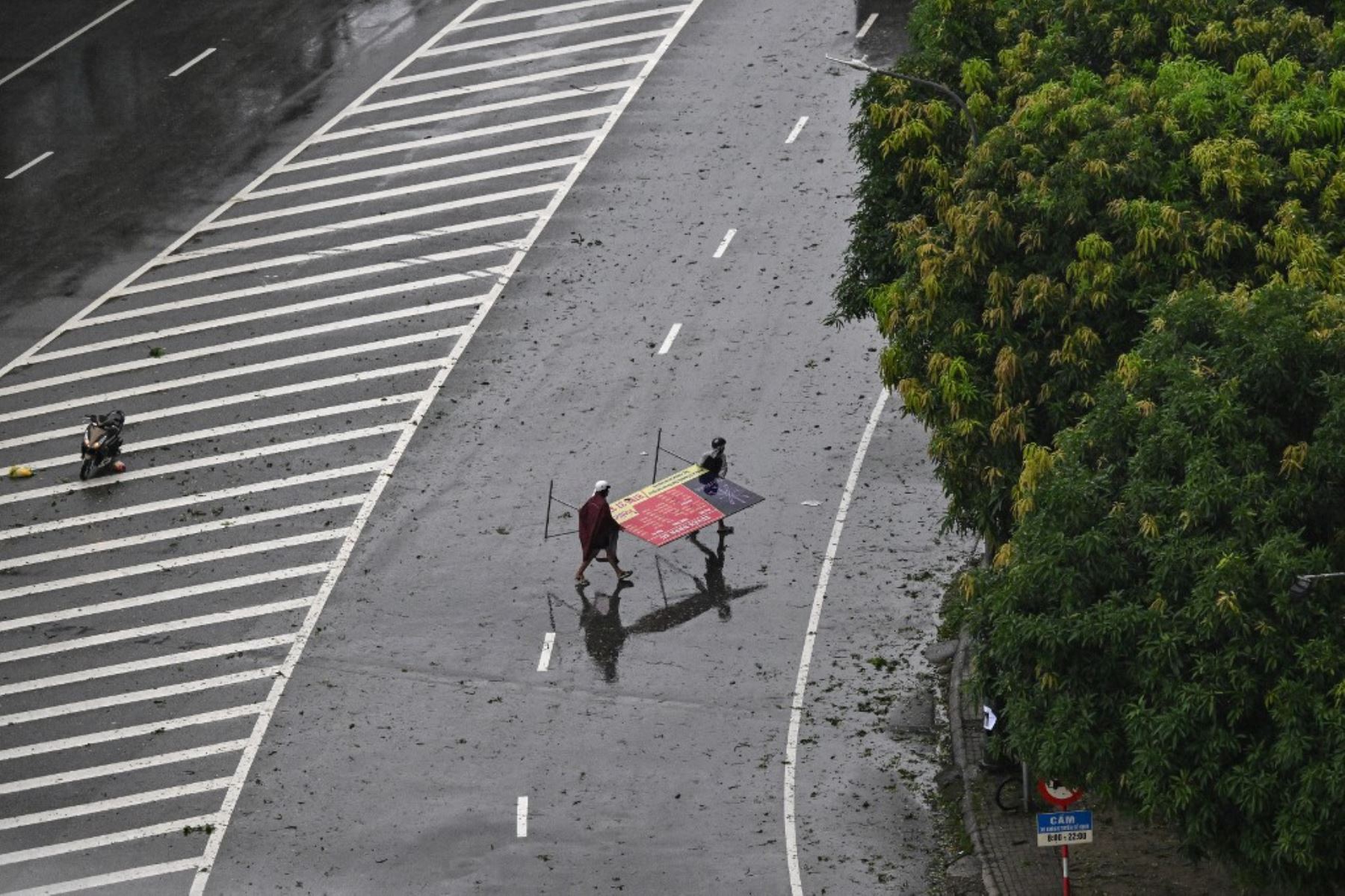 Hombres llevan en brazos un cartel publicitario que fue lanzado al aire en medio de una calle en la ciudad de Vinh, provincia de Nghe An, el 25 de agosto de 2025, ante la inminente llegada del tifón Kajiki, con vientos de unos 160 km/h. Foto: AFP
