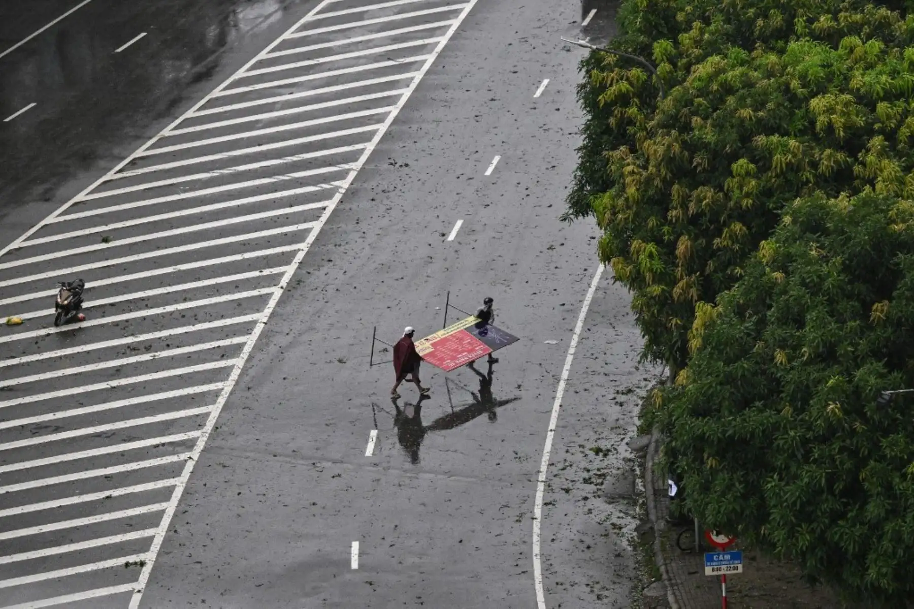 Hombres llevan en brazos un cartel publicitario que fue lanzado al aire en medio de una calle en la ciudad de Vinh, provincia de Nghe An, el 25 de agosto de 2025, ante la inminente llegada del tifón Kajiki, con vientos de unos 160 km/h. Foto: AFP