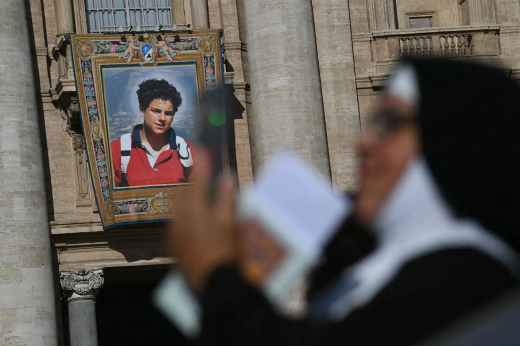 Un retrato del difunto adolescente italiano Carlo Acutis se exhibe en la fachada de la Basílica de San Pedro del Vaticano durante la Santa Misa por su canonización. El adolescente italiano, apodado "el Influencer de Dios", se convirtió en el primer santo milenial el domingo en una canonización a la que asistieron miles de peregrinos. Foto: AFP