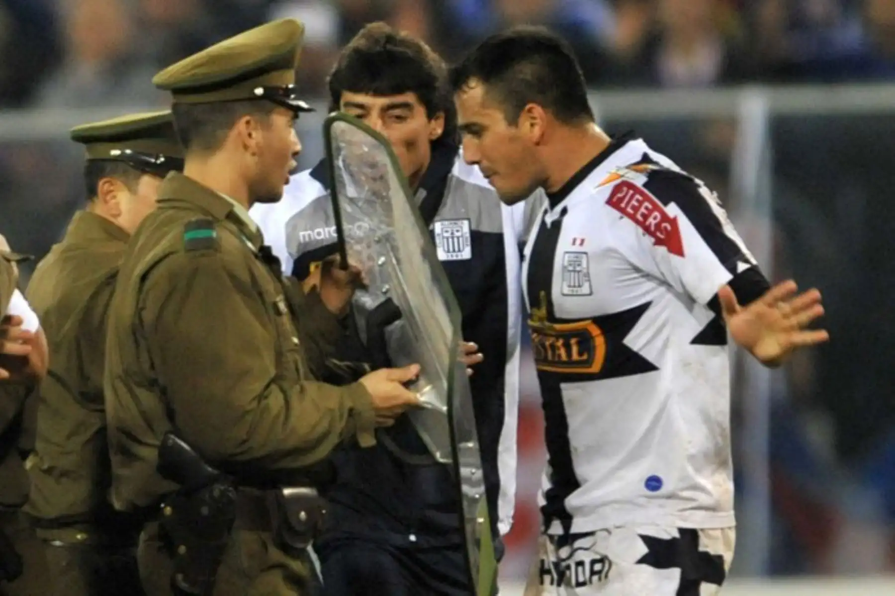 El futbolista Héctor Sosa, del Alianza Lima, discute con la policía mientras los agentes de seguridad protegen al árbitro Carlos Alfredo Vera durante los incidentes en el partido de la Copa Libertadores entre Alianza y la Universidad de Chile. Foto: AFP