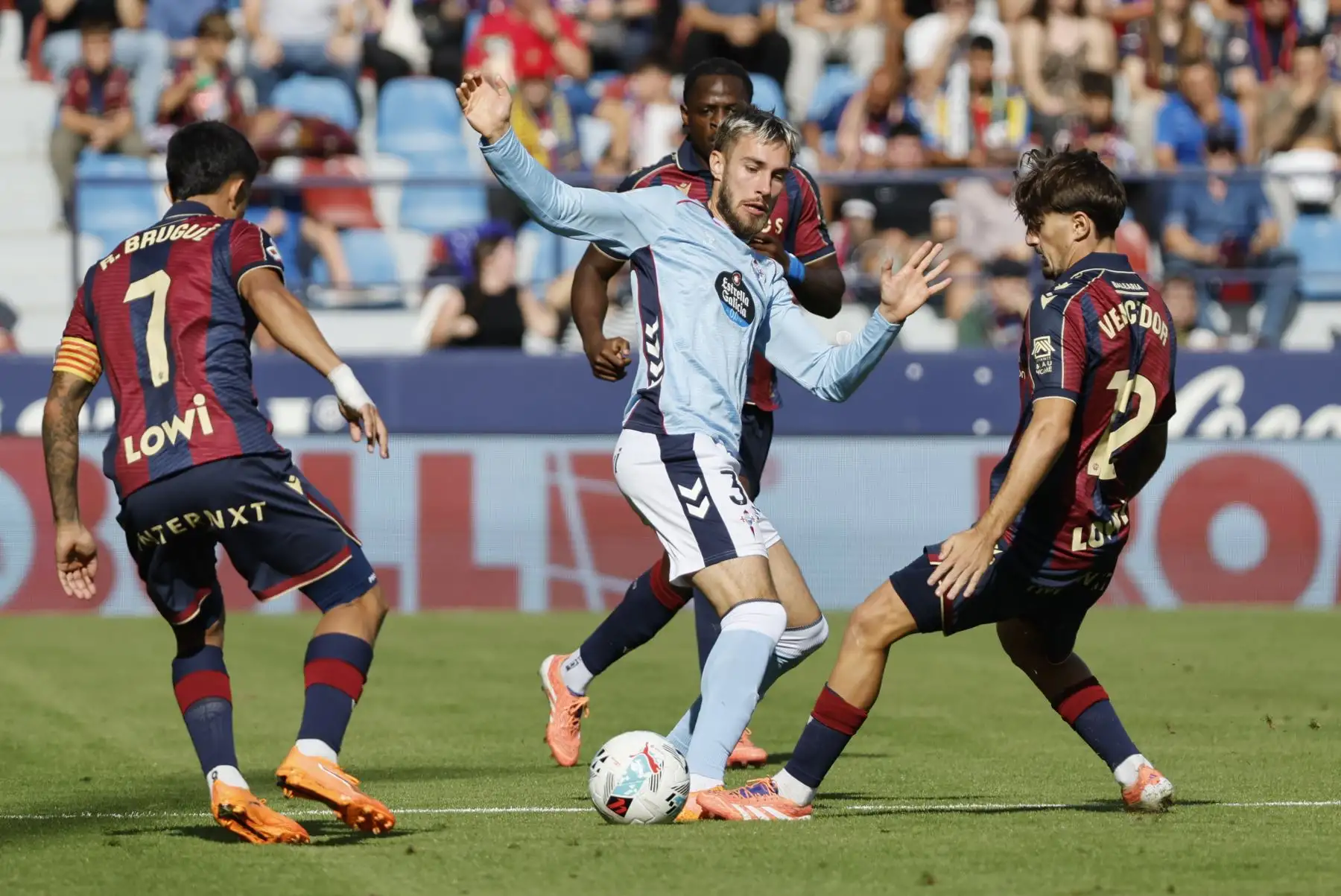 El defensa del Celta de Vigo Óscar Mingueza lucha por el balón con Roger Brugué y Unai Vencedor, del Levante, durante el partido correspondiente a la undécima jornada de LaLiga EA Sports disputado este domingo en el Ciutat de València. Foto: ANDINA/EFE