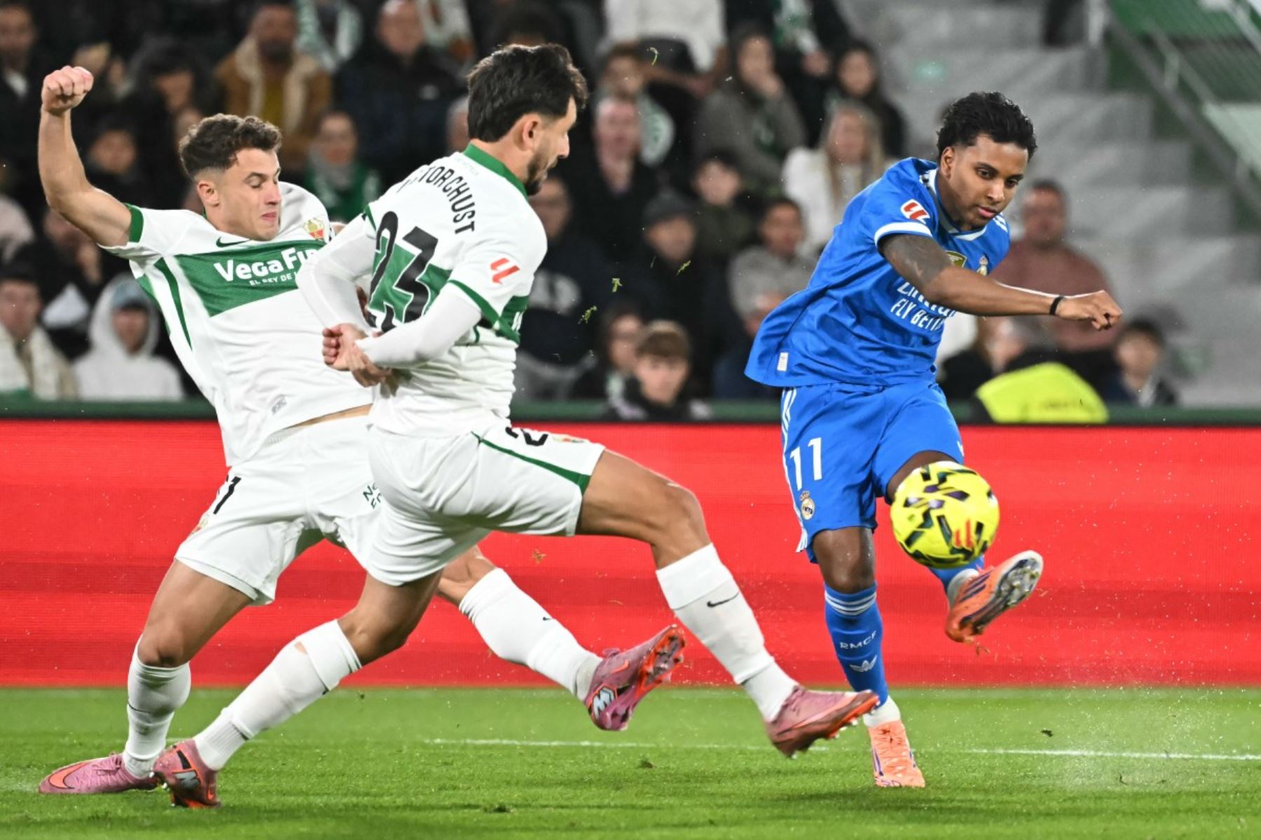 El defensor español #23 del Elche, Victor Chust (C), desafía al delantero brasileño del Real Madrid #11 Rodrygo durante el partido de fútbol de la liga española entre Elche CF y el Real Madrid CF en el Estadio Martínez Valero de Elche el 23 de noviembre de 2025. (Foto de JOSE JORDAN / AFP)
