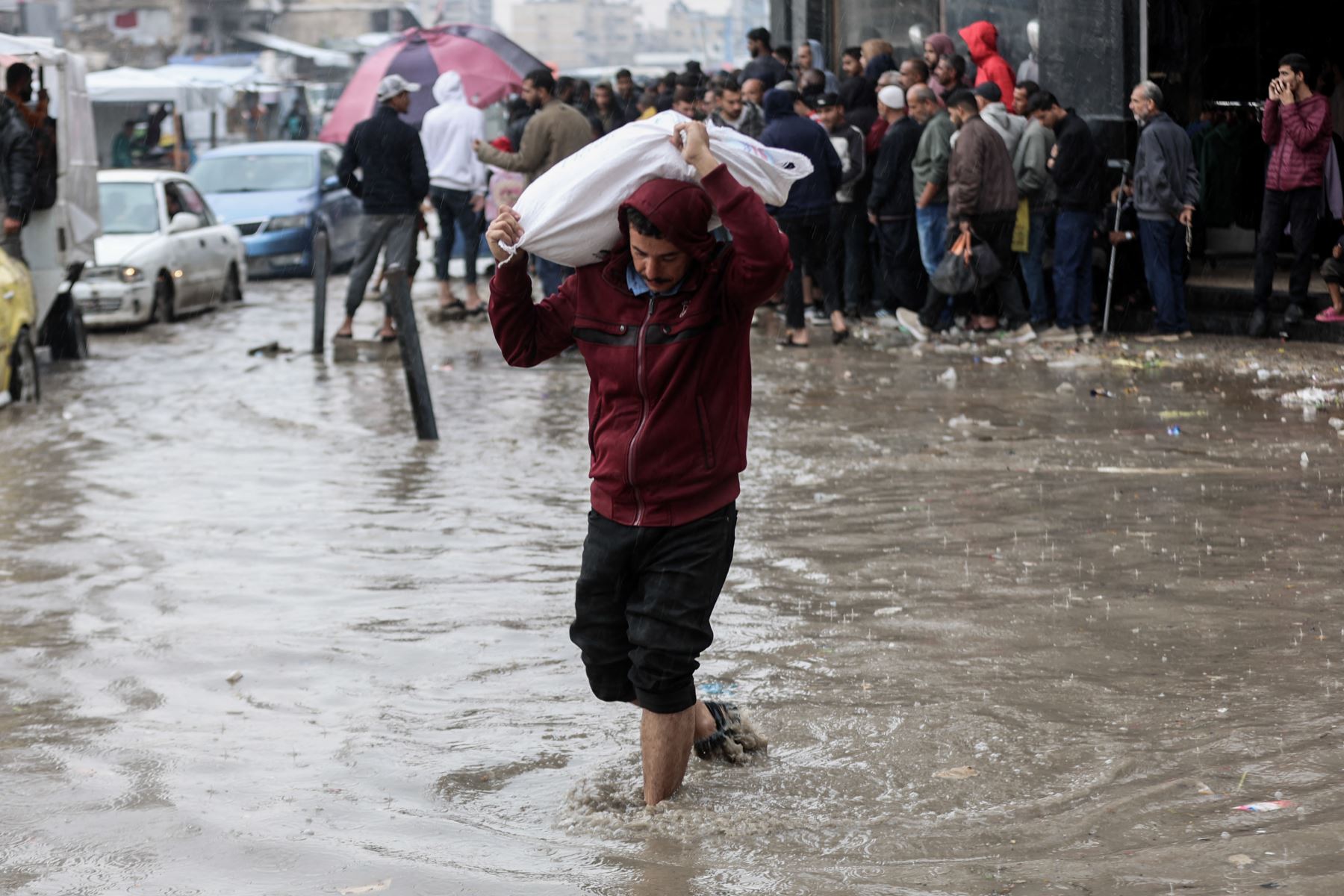 Un hombre carga un saco mientras camina entre las aguas inundadas en un campamento improvisado que alberga a palestinos desplazados tras las fuertes lluvias en la ciudad de Gaza el 25 de noviembre de 2025. La Franja de Gaza ha quedado prácticamente reducida a escombros tras dos años de combates. Foto: AFP