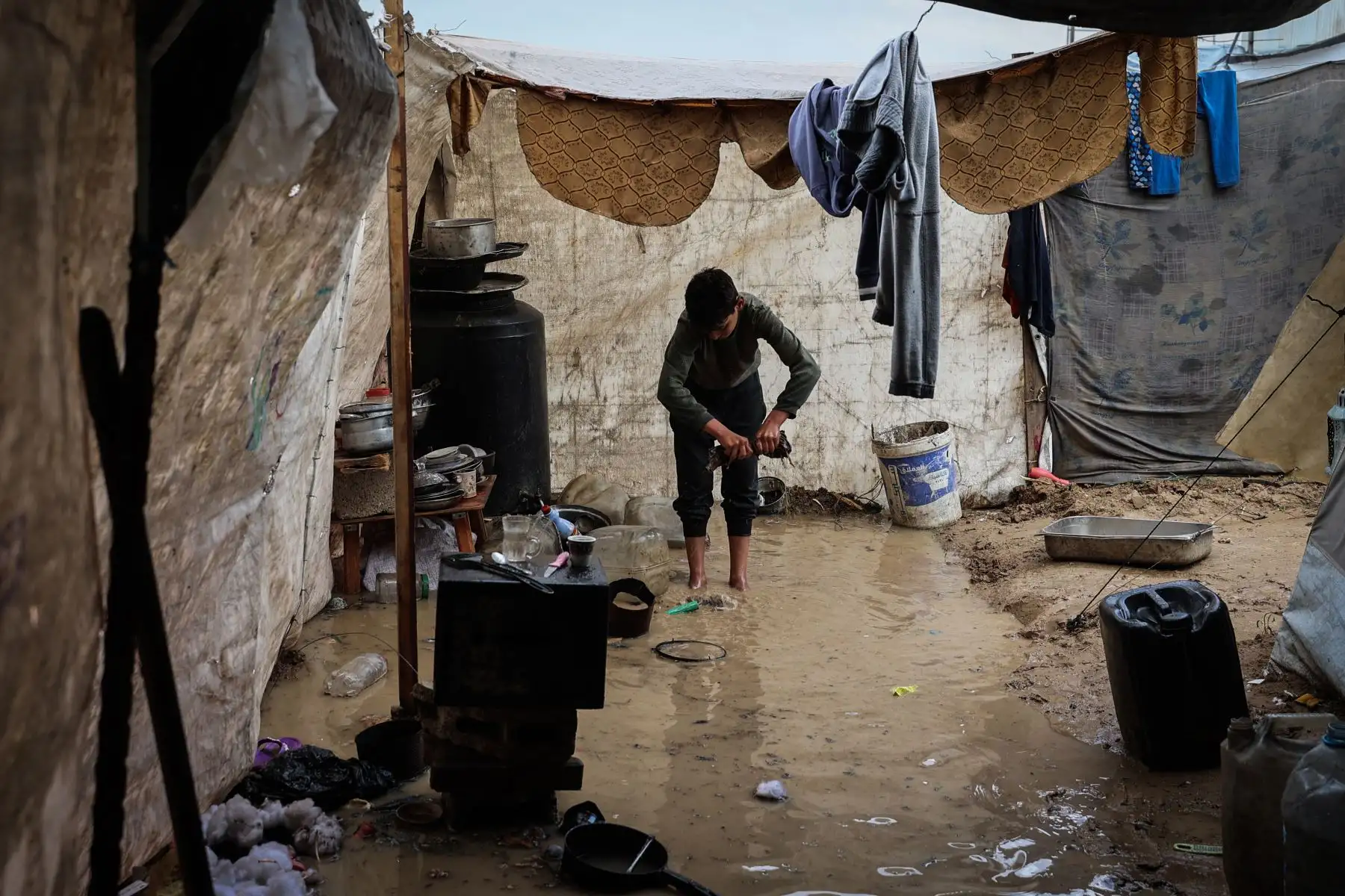 Un niño escurre una prenda de ropa después de que las fuertes lluvias inundaran un campamento improvisado que albergaba a palestinos desplazados en el campo de refugiados de Maghazi, en el centro de la Franja de Gaza, el 25 de noviembre de 2025. Foto: AFP