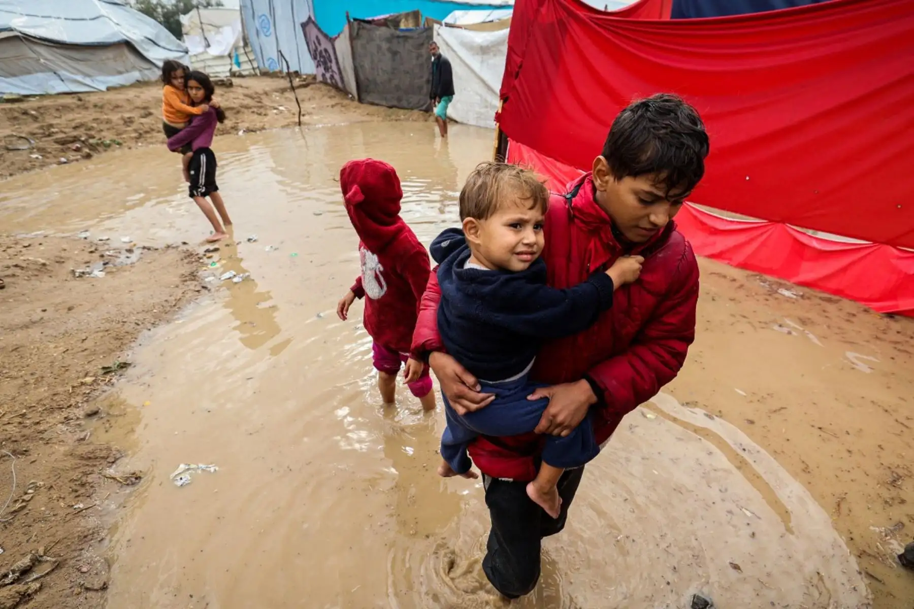 Niños palestinos caminan entre las aguas inundadas tras las fuertes lluvias en un campamento improvisado que alberga a palestinos desplazados en el campo de refugiados de Maghazi, en el centro de la Franja de Gaza, el 25 de noviembre de 2025. Foto: AFP