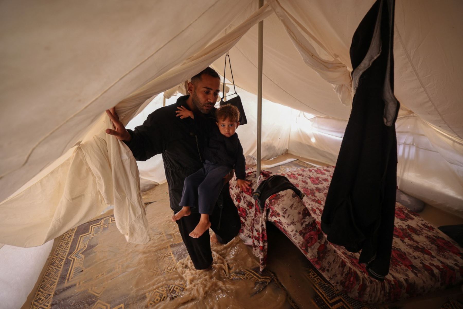 Un hombre lleva a su hijo dentro de una tienda de campaña después de que las fuertes lluvias inundaran un campamento improvisado que albergaba a palestinos desplazados en el campo de refugiados de Maghazi, en el centro de la Franja de Gaza, el 25 de noviembre de 2025. Foto: AFP