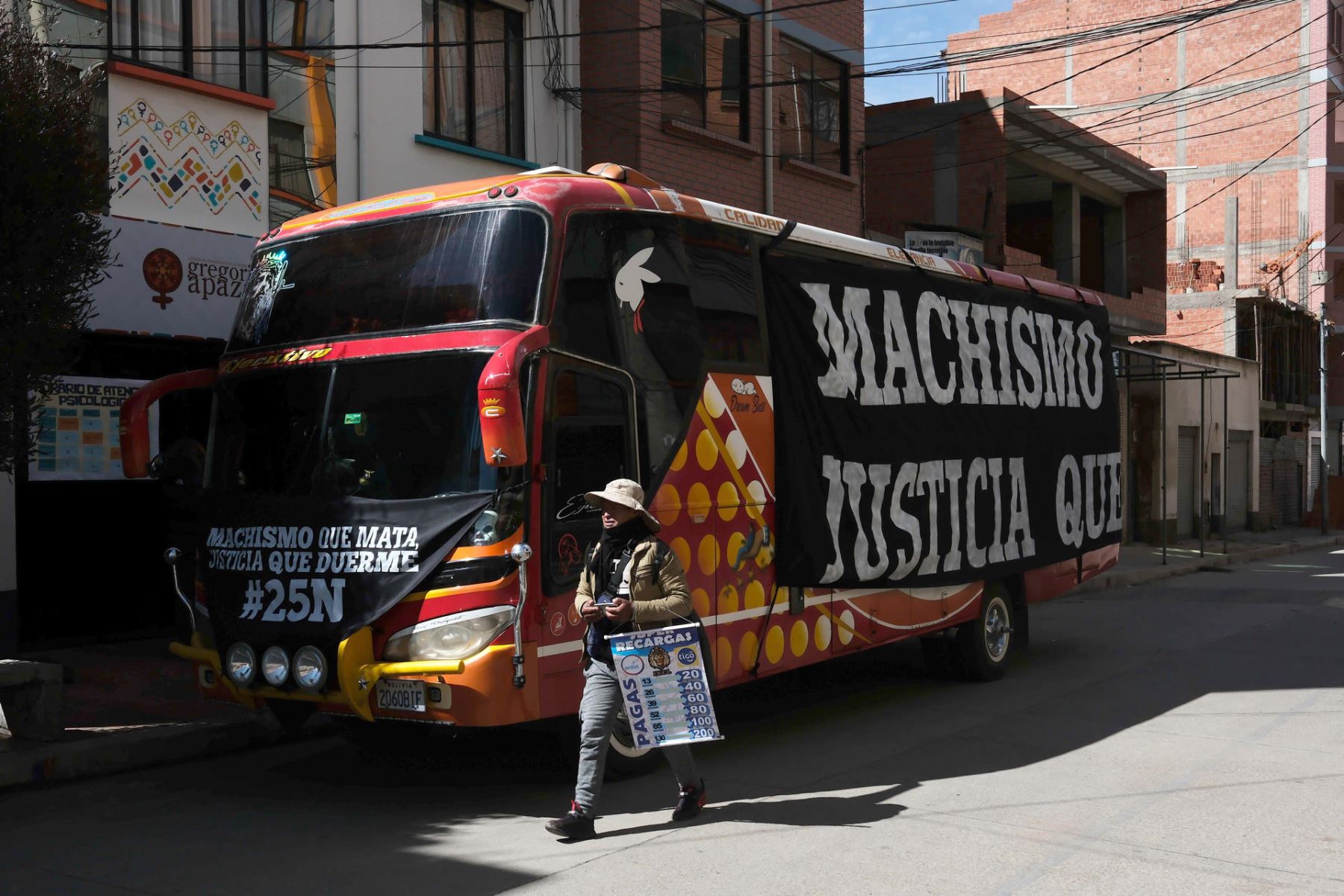 Una persona camina delante de un autobús con mensajes en contra de la violencia machista en El Alto, Bolivia. El bus fue ocupado por mujeres y recorrió diferentes zonas de la ciudad para informar sobre cómo prevenir la violencia machista en el país, en conmemoración del Día Internacional de la Eliminación de la Violencia contra la Mujer. Foto: EFE