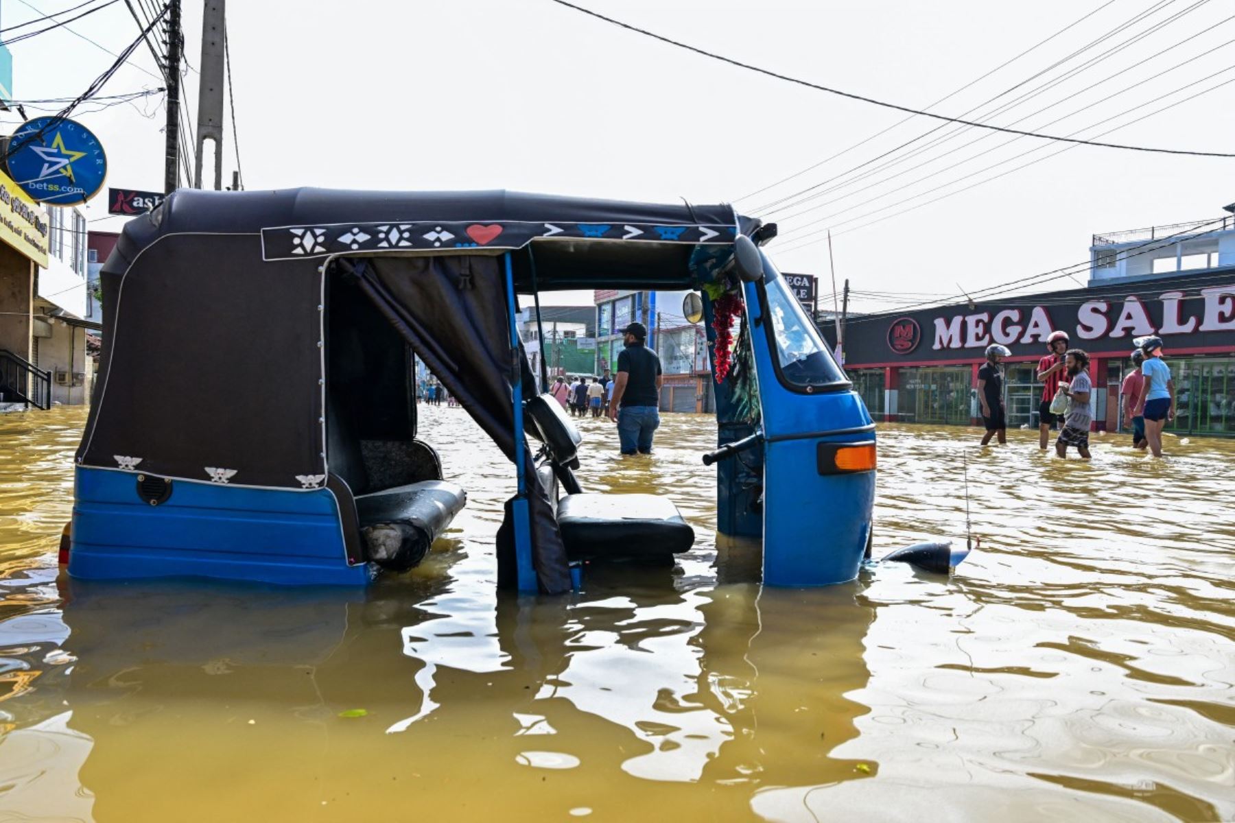 Un auto rickshaw se encuentra varado mientras la gente camina por una calle inundada después de fuertes lluvias en Wellampitiya, en las afueras de Colombo. AFP