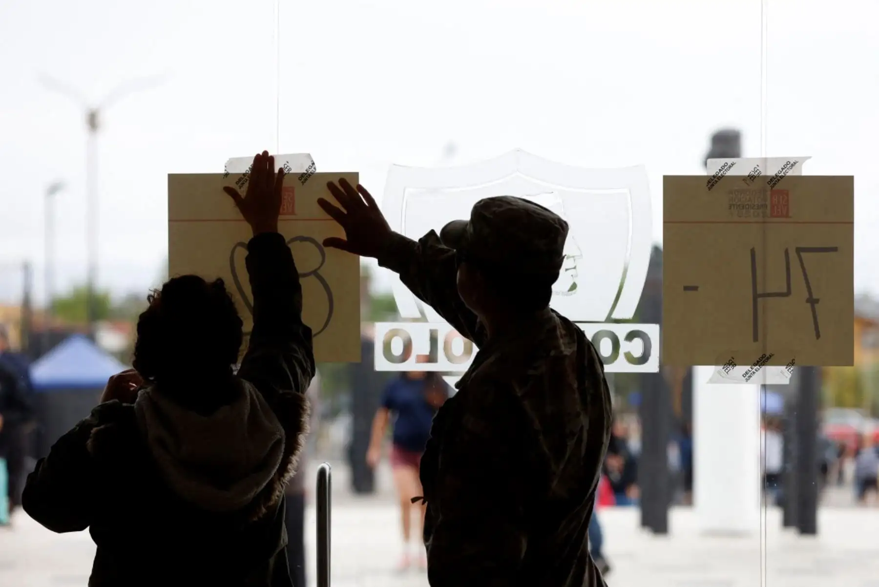 Un soldado y un soman colocaron un cartel durante la segunda sección presidencial en el Estadio Monumental Colo-Colo en Santiago, Chile, el 14 de diciembre de 2025. Los chilenos se dirigen a las urnas para una resección presidencial entre Jeannette Jara, una comunista respaldada por una amplia coalición de izquierda, y José Antonio Kast, un devoto político de extrema derecha que promete una línea dura en seguridad y migración. (Foto de Raúl BRAVO / AFP)