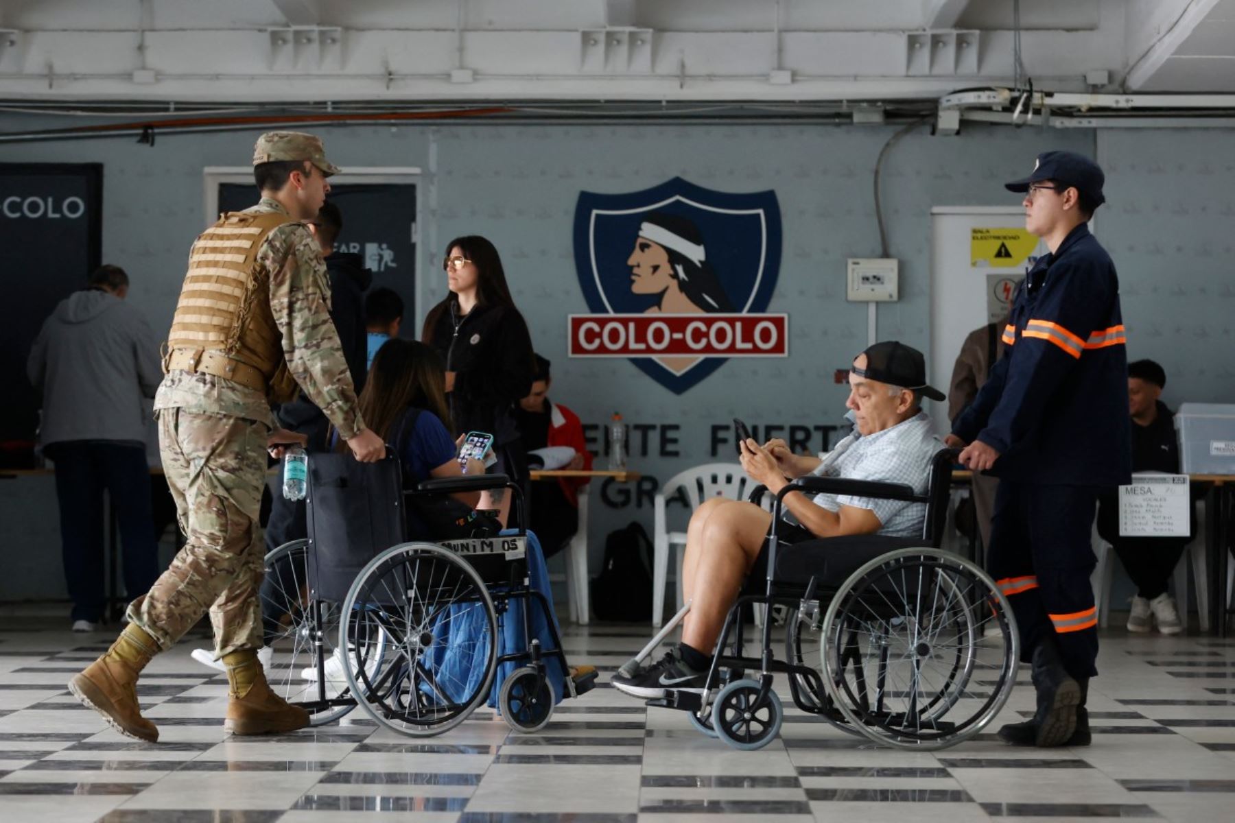 Un soldado empuja a una mujer en una silla de ruedas durante la segunda sección presidencial en el Estadio del club Monumental Colo-Colo en Santiago, Chile, el 14 de diciembre de 2025. Los chilenos se dirigen a las urnas para una resección presidencial entre Jeannette Jara, una comunista respaldada por una amplia coalición de izquierda, y José Antonio Kast, un devoto político de extrema derecha que promete una línea dura en seguridad y migración. (Foto de Raúl BRAVO / AFP)