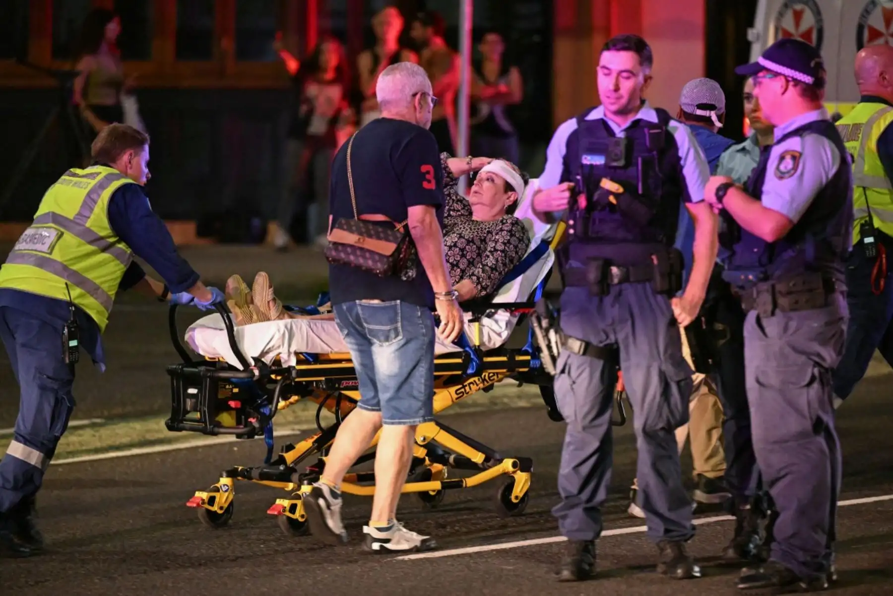 Los trabajadores de la salud trasladan a una mujer en una camilla a una ambulancia después de un incidente de tiroteo en Bondi Beach en Sydney el 14 de diciembre de 2025. La policía australiana dijo que dos personas estaban bajo custodia después de informes de múltiples disparos el 14 de diciembre en la famosa playa Bondi de Sydney, instando al público a refugiarse. (Foto de Saeed KHAN / AFP)