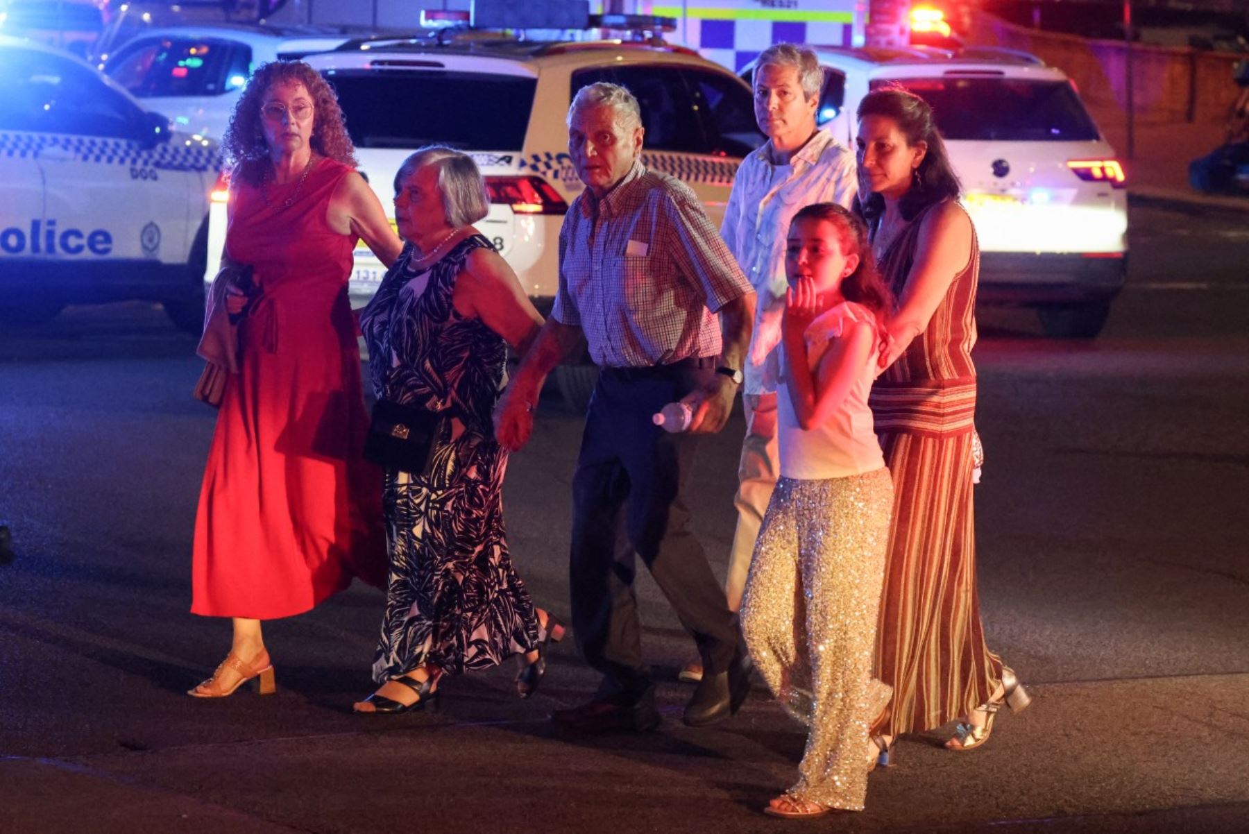 La gente cruza una calle junto a los vehículos policiales después de un incidente de tiroteo en Bondi Beach en Sydney el 14 de diciembre de 2025. La policía australiana dijo que dos personas estaban bajo custodia después de informes de múltiples disparos el 14 de diciembre en la famosa playa Bondi de Sydney, instando al público a refugiarse. (Foto de DAVID GRAY / AFP)