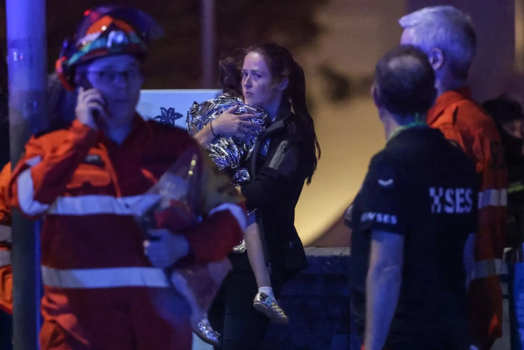 Una mujer sostiene a un niño en una manta después de un incidente de tiroteo en Bondi Beach en Sydney el 14 de diciembre de 2025. La policía australiana dijo que dos personas estaban bajo custodia después de informes de múltiples disparos el 14 de diciembre en la famosa playa Bondi de Sydney, instando al público a refugiarse. (Foto de DAVID GRAY / AFP)