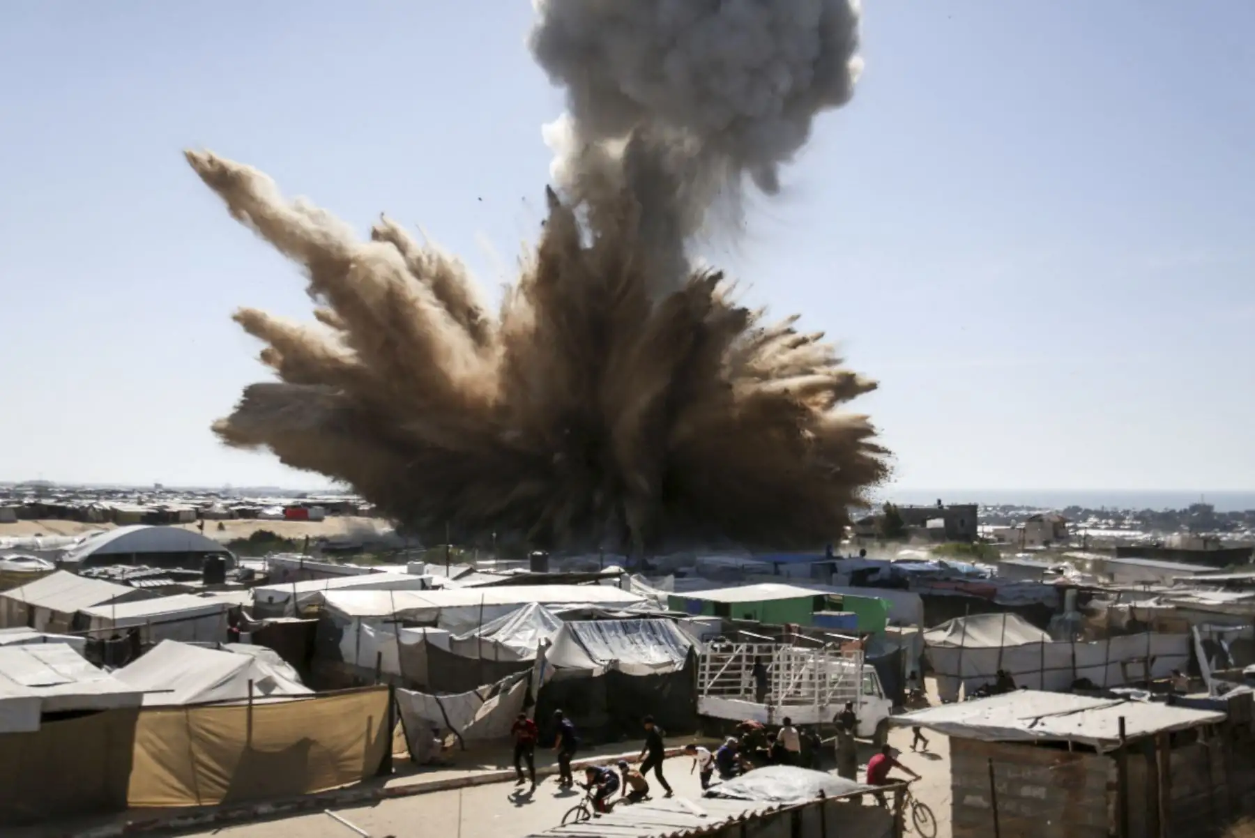 La gente corre para cubrirse mientras una pluma de humo se eleva sobre las tiendas de campaña en un campamento para palestinos desplazados en el norte de Khan Yunis, en el sur de la Franja de Gaza, durante un ataque israelí el 19 de abril de 2025. (Foto de AFP)