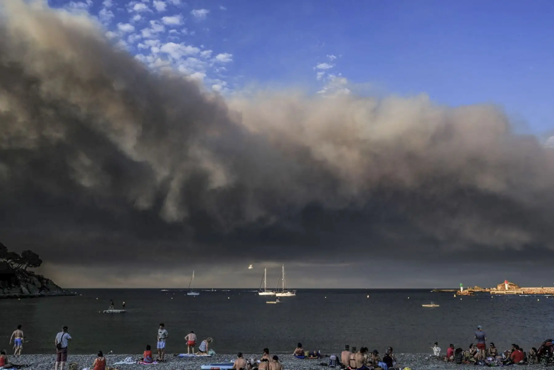 Los turistas se sientan en la playa mientras el humo de los incendios forestales que se enfurecen en el departamento de Aude se ve desde la costa mediterránea en Banyuls-sur-Mer, al suroeste de Francia, el 5 de agosto de 2025. Un incendio que estalló el 5 de agosto de 2025 por la tarde en Ribaute (Aude) ha quemado 4.000 hectáreas de bosque y matorrales en solo unas pocas horas antes de llegar al pueblo de Saint-Laurent-de-la-Cabrerisse, donde se quemaron casas. (Foto de OLIVIER CHASSIGNOLE / AFP)