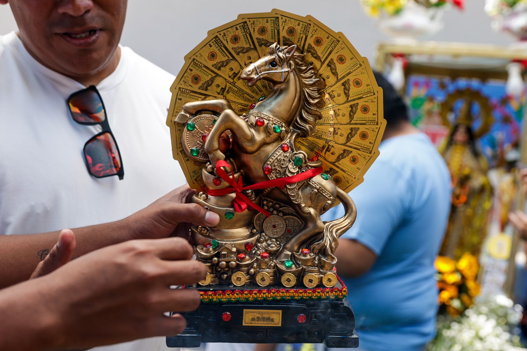 Una figura dorada es presentada como símbolo de prosperidad y abundancia, uno de los pedidos más recurrentes entre los asistentes. Estas piezas suelen ser bendecidas durante rituales ya que estos objetos, según la creencia, actúan como representaciones materiales de los deseos que se buscan concretar con fe y constancia. Foto: ANDINA/Luis Iparraguirre