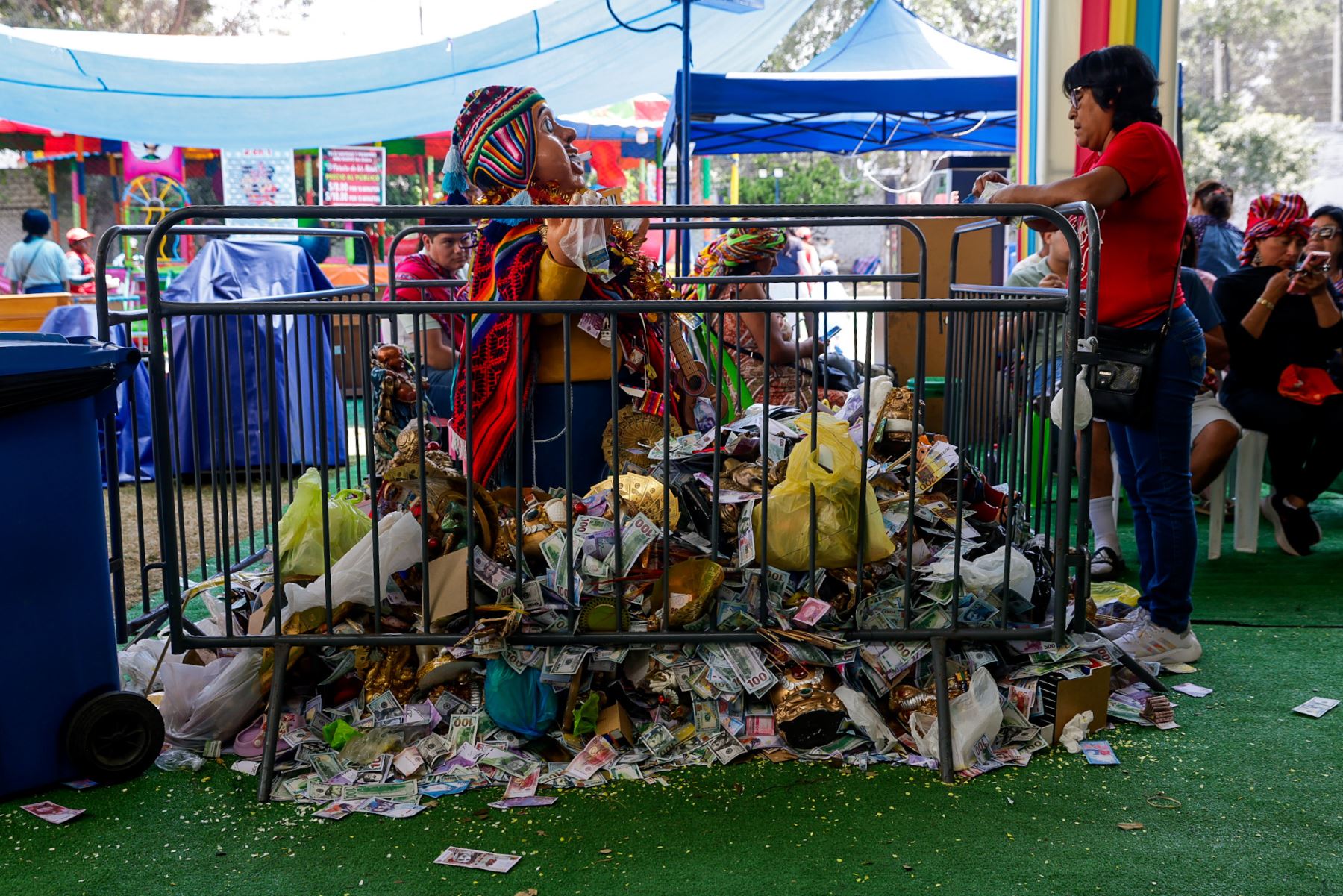 Un Ekeko de gran tamaño permanece cubierto de billetes simbólicos, fotografías y ofrendas dejadas por los visitantes. La acumulación representa pedidos colectivos de abundancia y prosperidad, una práctica recurrente en la feria, donde los asistentes depositan sus deseos con la esperanza de atraer un mejor futuro. Foto: ANDINA/Luis Iparraguirre