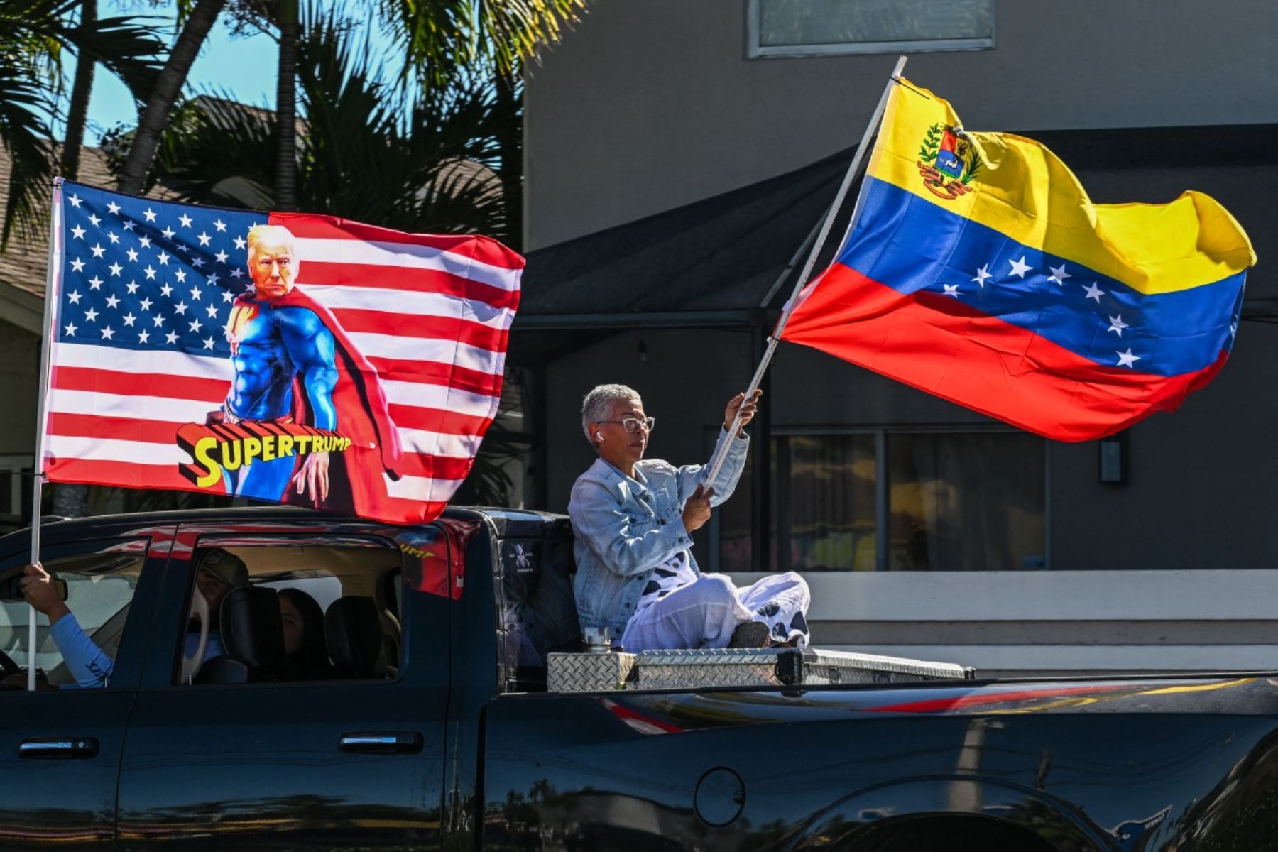 Un manifestante ondea la bandera de Venezuela desde una camioneta, mientras otro exhibe un estandarte con la imagen del presidente estadounidense Donald Trump, en Doral, cerca de Miami. La escena refleja la euforia y el respaldo de parte de la diáspora venezolana tras la captura de Nicolás Maduro por fuerzas de Estados Unidos. Foto: AFP