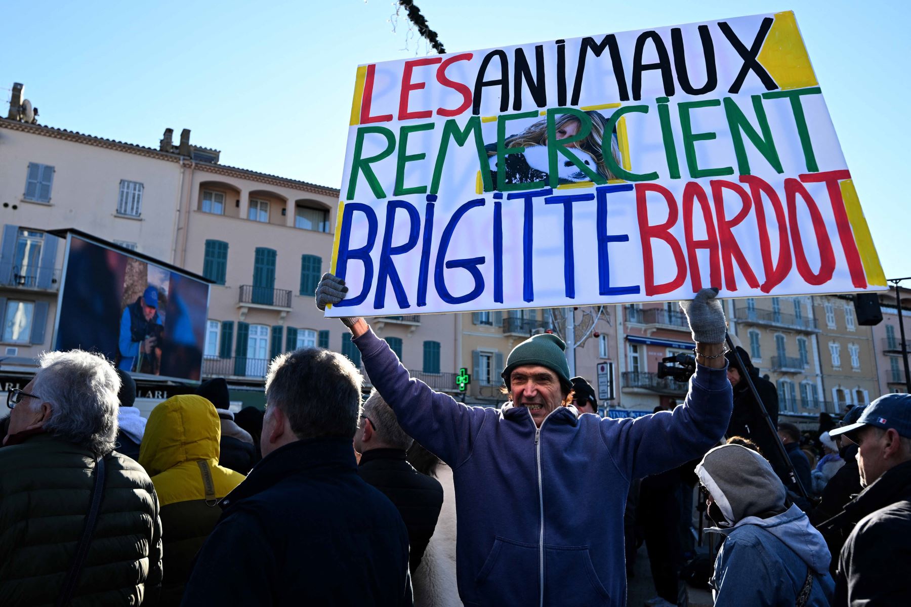 El activista francés Jean-Baptiste Redde, también conocido como Voltuan, sostiene una pancarta con la leyenda "Los animales agradecen a Brigitte Bardot" mientras dolientes y seguidores observan en una pantalla la transmisión en vivo del funeral de la fallecida actriz francesa Brigitte Bardot, en la iglesia de Notre-Dame de l