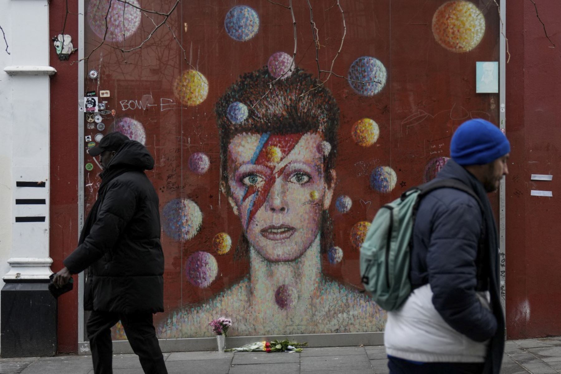 La gente pasa junto a un mural del difunto icono del pop británico David Bowie creado por el artista callejero australiano James Cochran, también conocido como Jimmy C, en Brixton, al sur de Londres, el 10 de enero de 2026, en el décimo aniversario de la muerte del músico. (Foto de CARLOS JASSO / AFP)