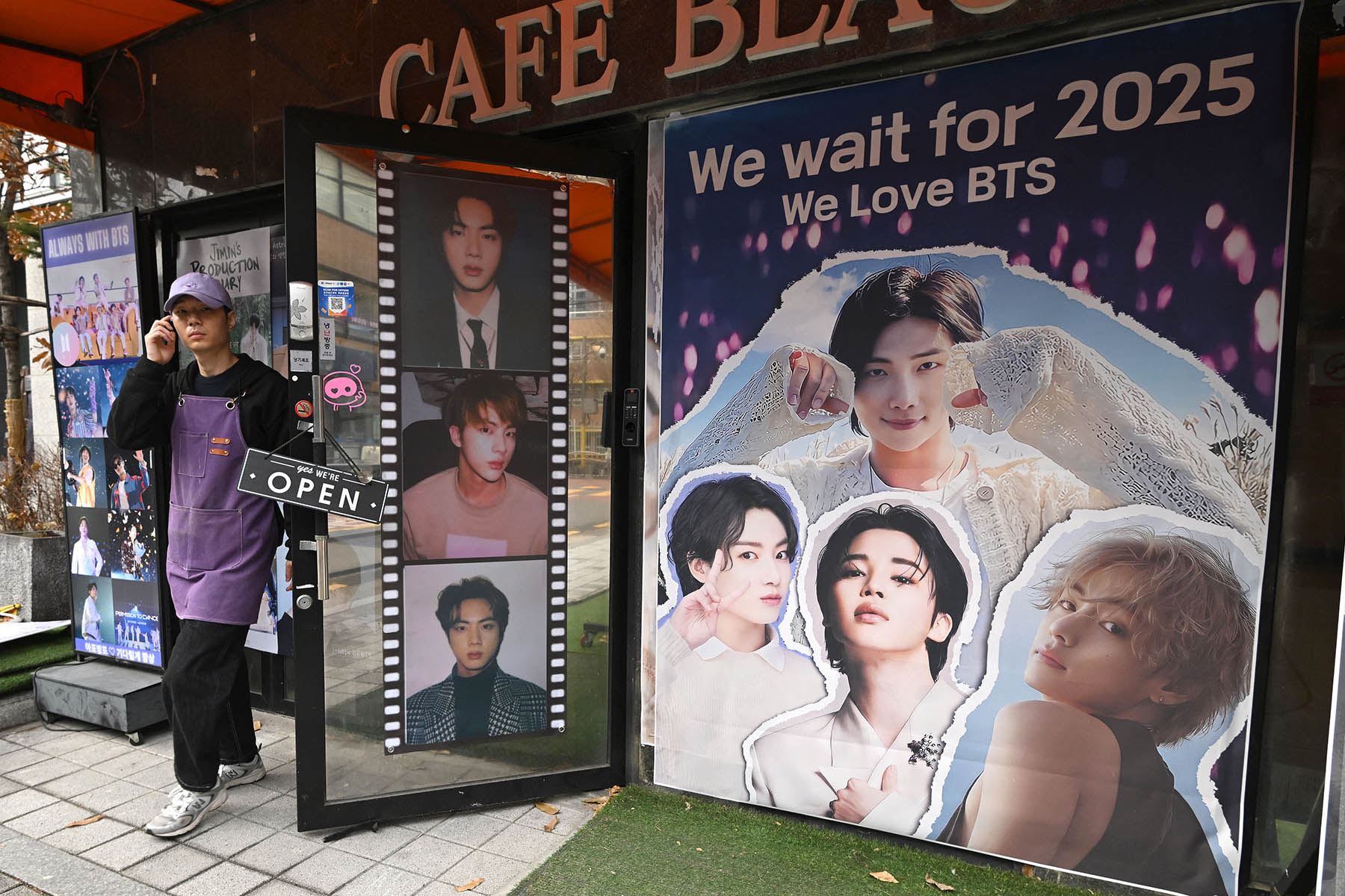 Un hombre pasa junto a un cartel con imágenes de los miembros del grupo surcoreano de K-pop BTS frente a una cafetería en Seúl el 12 de diciembre de 2023. Foto: AFP