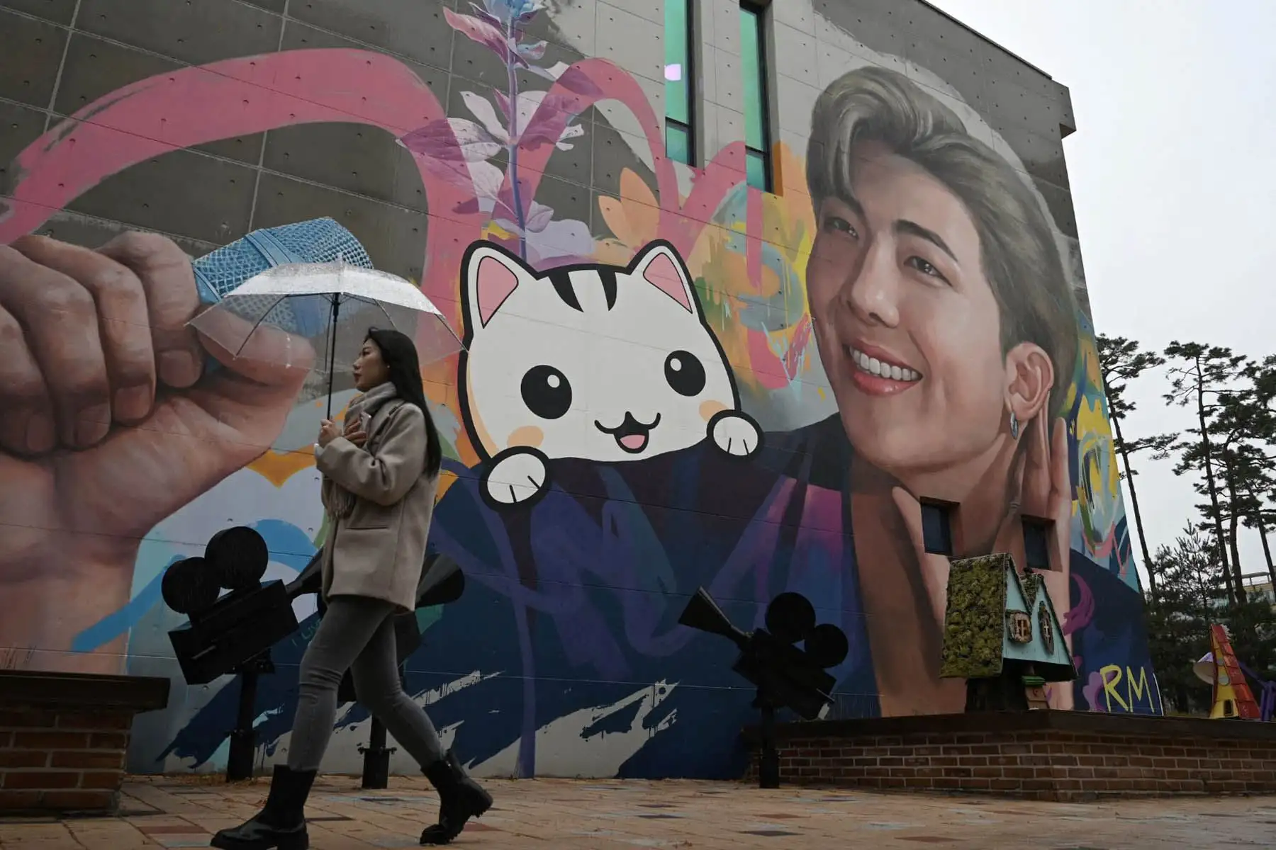 Una mujer pasa junto a un mural que representa a RM, miembro del grupo de K-pop BTS, en Goyang, al noroeste de Seúl, el 11 de diciembre de 2023. Foto: AFP