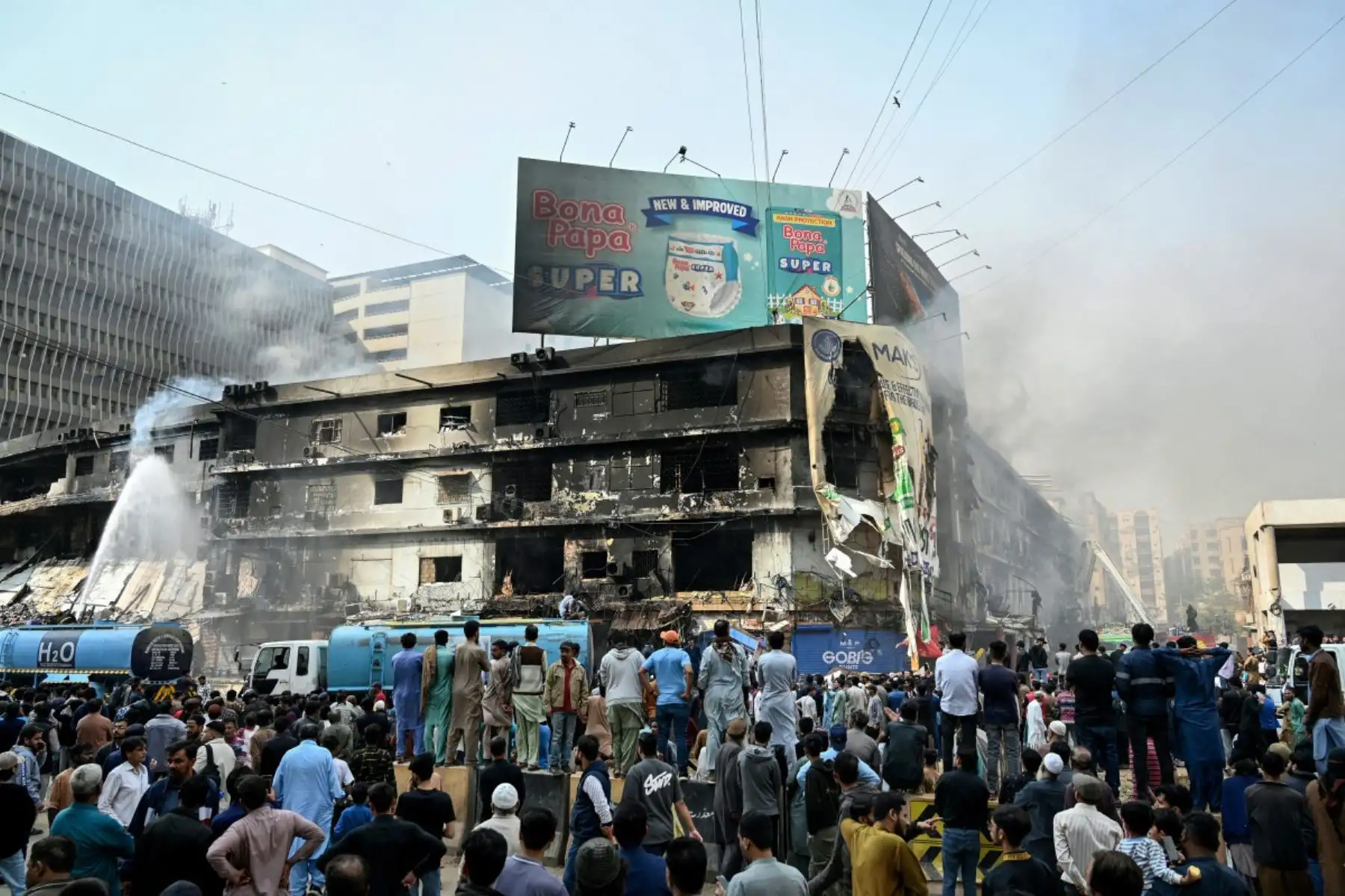 La gente observa cómo los bomberos realizan una operación de enfriamiento en una estructura quemada después de un gran incendio en un centro comercial en Karachi el 19 de enero de 2026. Foto: ANDINA/AFP
