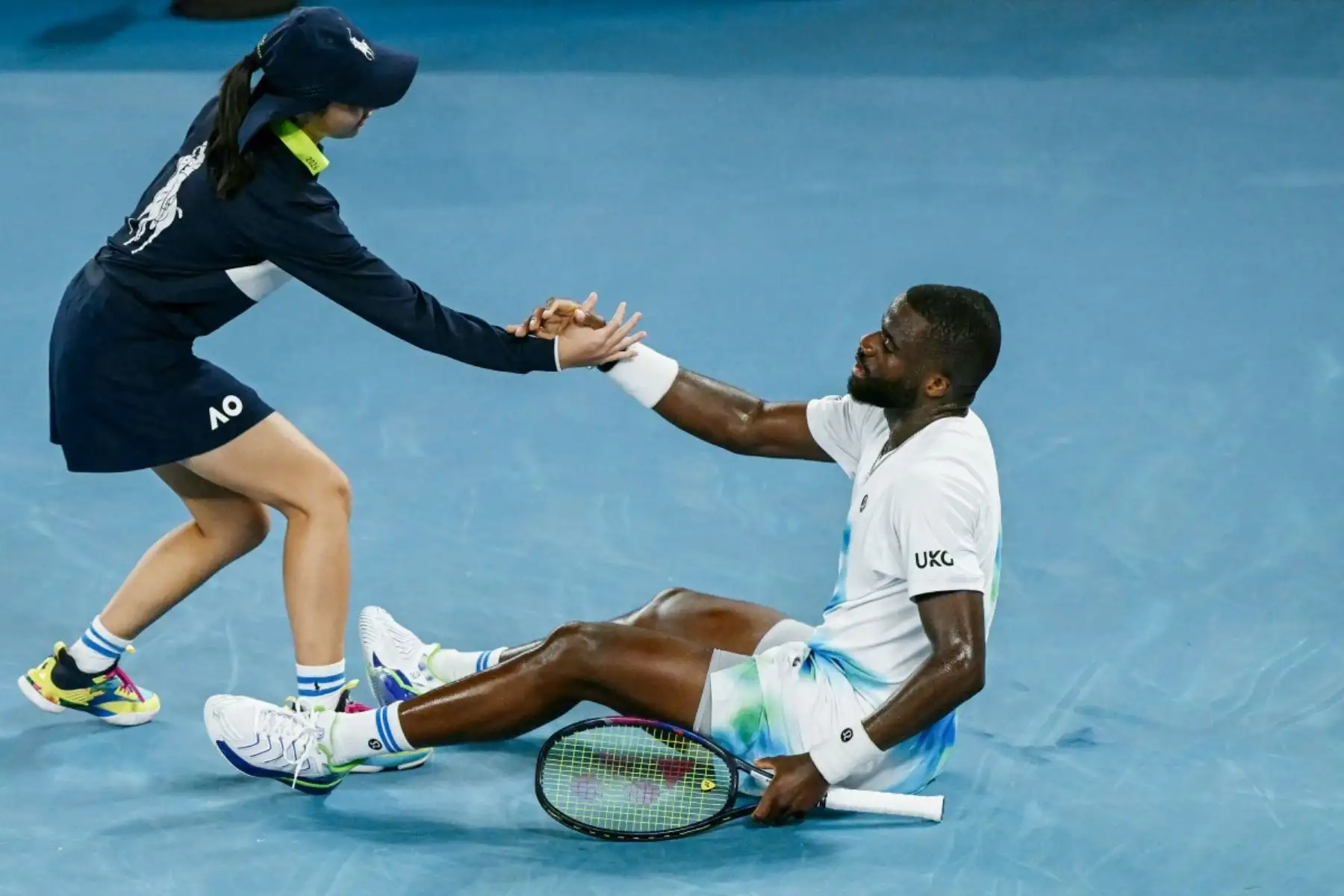 Frances Tiafoe, de EE. UU., está siendo ayudado por un niño de pelota después de caer en la cancha durante su partido individual masculino contra Alex De Minaur de Australia en el sexto día del torneo de tenis Abierto de Australia en Melbourne el 23 de enero de 2026. (Foto de WILLIAM WEST / AFP)