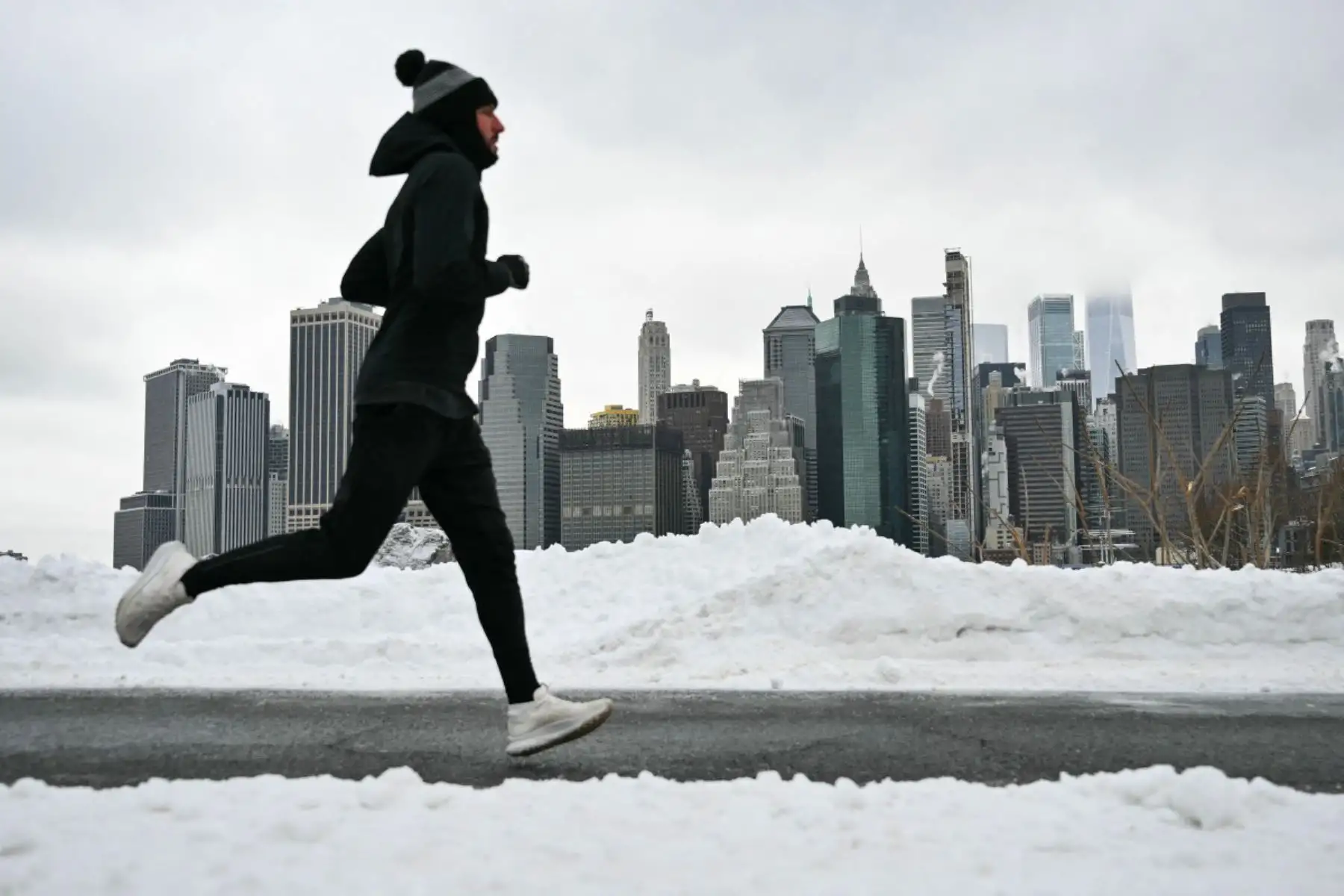 El horizonte del Bajo Manhattan se ve al fondo mientras un hombre corre por un sendero en el barrio de Brooklyn de la ciudad de Nueva York. Una tormenta monstruosa que azotaba Estados Unidos causó la muerte de al menos 11 personas el lunes, lo que provocó advertencias para evitar circular por carretera, cancelaciones masivas de vuelos y cortes de electricidad tras un fin de semana desastroso. 
Foto: AFP