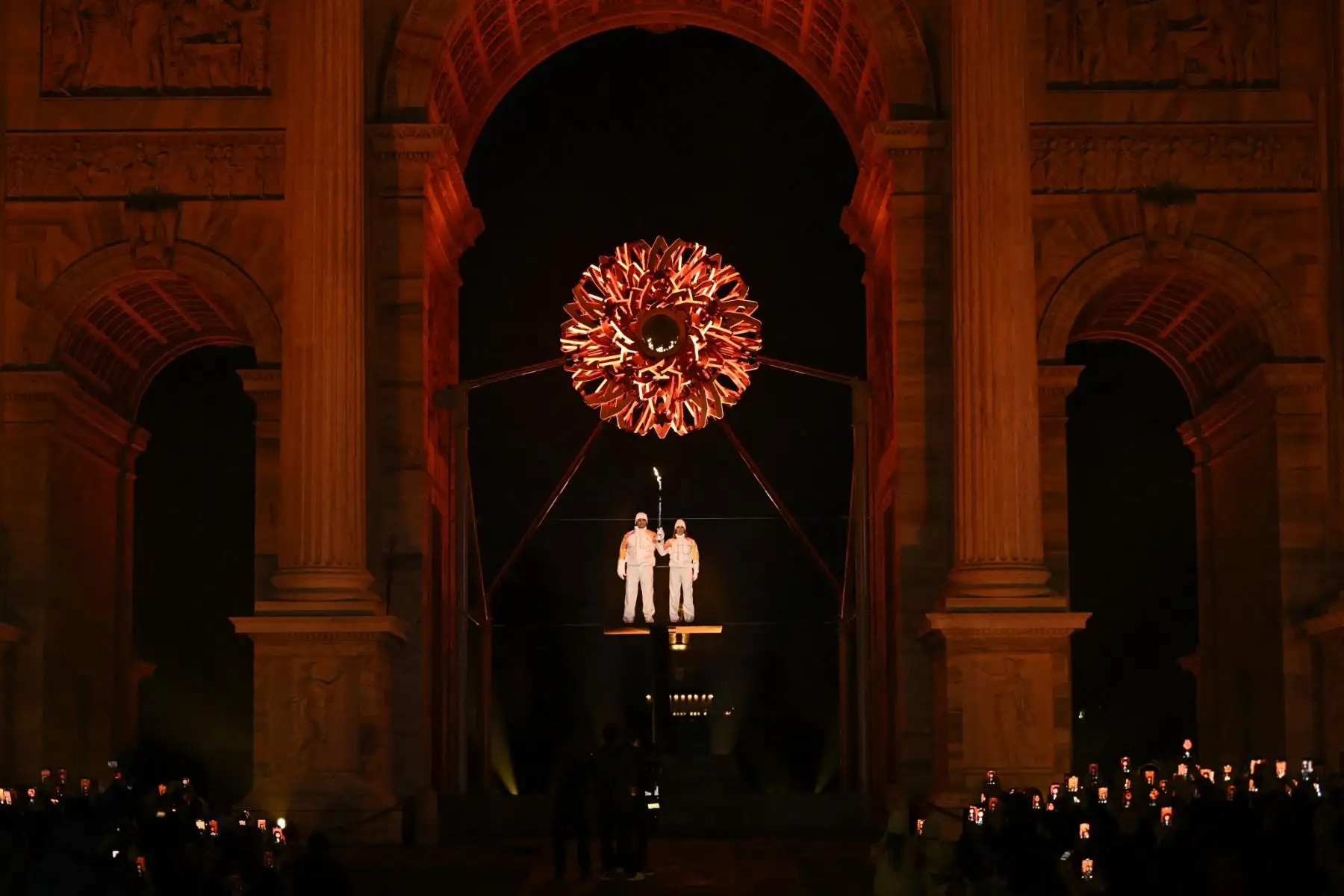 El italiano Alberto Tomba (izq.) sostiene la antorcha olímpica bajo el pebetero durante la ceremonia de apertura de los Juegos Olímpicos de Invierno Milano Cortina 2026 junto al monumento Arco della Pace en Milán, norte de Italia, el 6 de febrero de 2026. (Foto de JULIEN DE ROSA / AFP)
