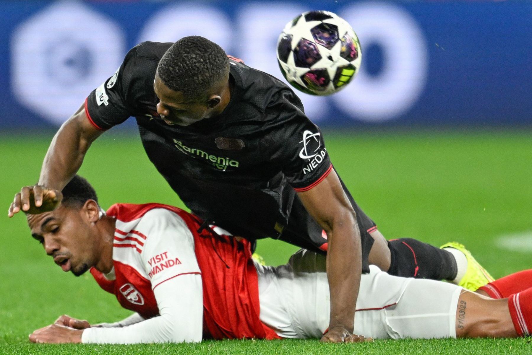 El delantero camerunés  del Bayer Leverkusen, Christian Kofane, cae sobre el defensa brasileño  del Arsenal, Gabriel Magalhaes, durante el partido de ida de los octavos de final de la UEFA Champions League, Bayer 04 Leverkusen vs Arsenal. AFP