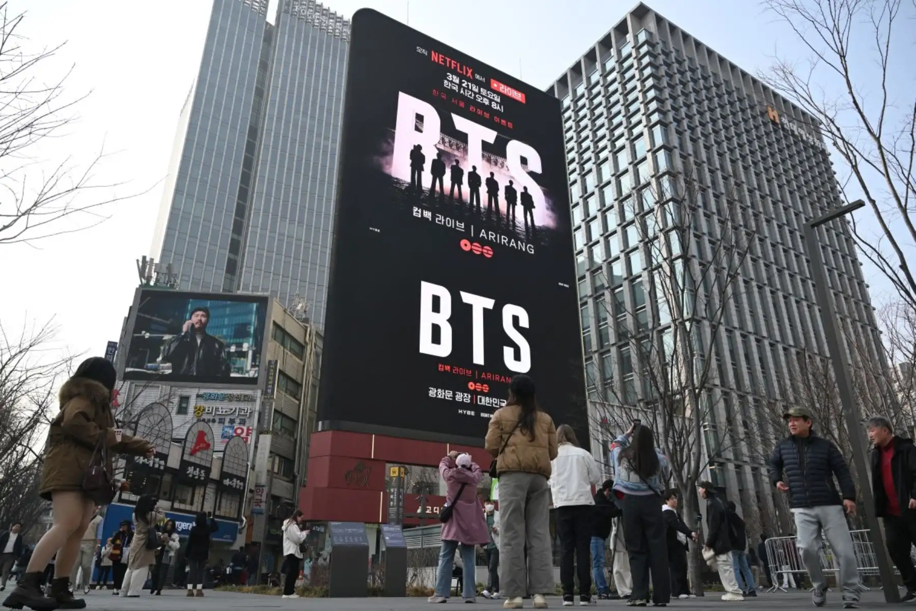 Varias personas pasan junto a una valla publicitaria que promociona el concierto de regreso del grupo de K-pop BTS en la plaza Gwanghwamun de Seúl. Foto: AFP