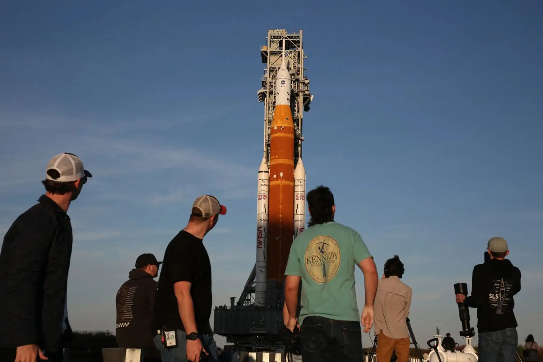 Miembros de la prensa observan cómo la plataforma de lanzamiento móvil 1, que contiene el enorme cohete Artemis II del Sistema de Lanzamiento Espacial (SLS) y la nave espacial Orion, regresa al Edificio de Ensamblaje de Vehículos desde la Plataforma de Lanzamiento 39B en el Centro Espacial Kennedy al anochecer en Cabo Cañaveral, Florida. Foto: ANDINA/AFP