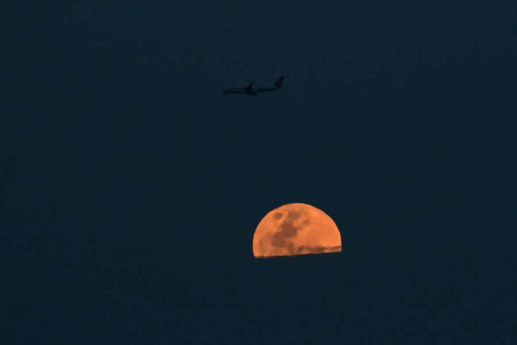Un avión de pasajeros sobrevuela la Ciudad de Panamá mientras una luna llena rosada se eleva. Foto: ANDINA/AFP