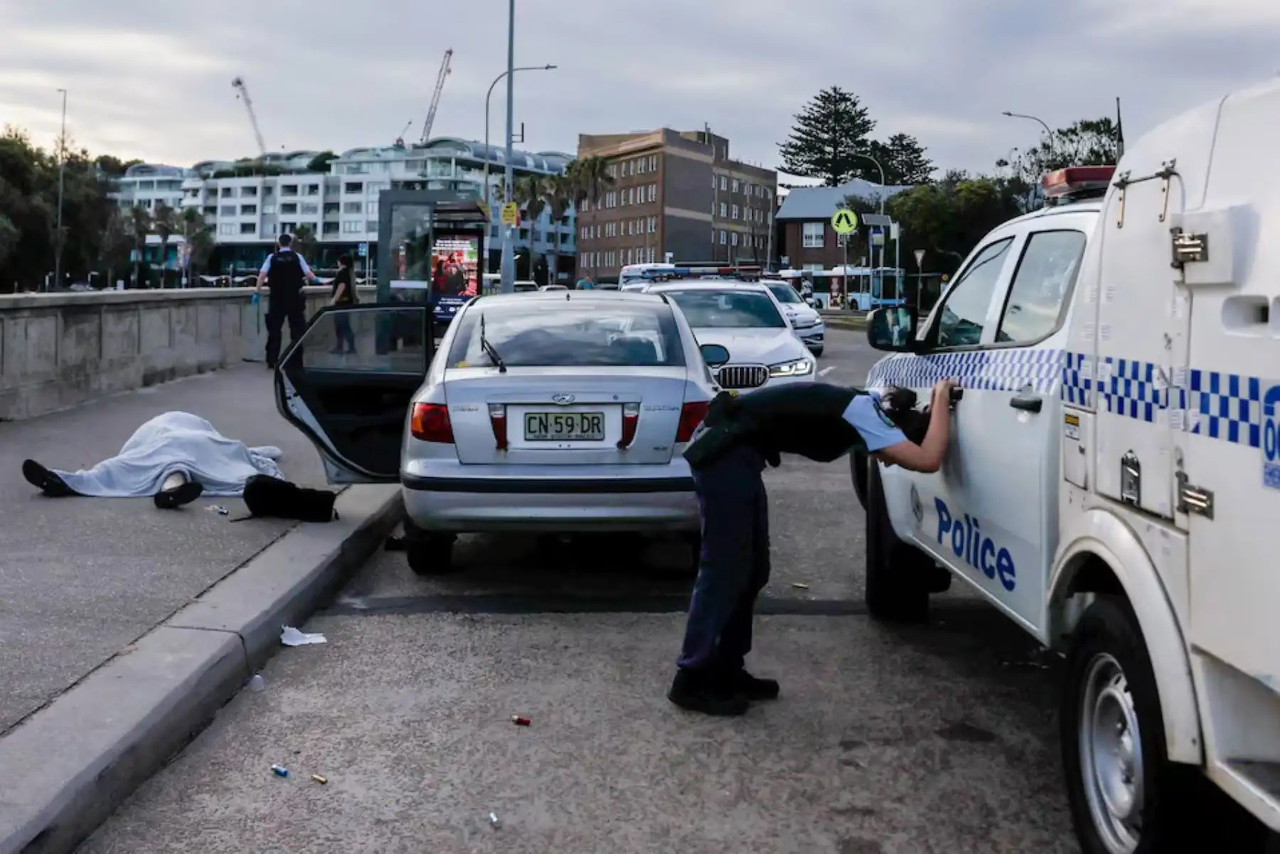 Un agente de policía, visiblemente afectado, se inclina junto a los cuerpos de Boris y Sofía Gurman, de 69 y 61 años respectivamente. Durante el atentado terrorista de Bondi Beach, la pareja perdió la vida al intentar desarmar a uno de los tiradores. Sídney, Australia. Foto: Edwina Pickles