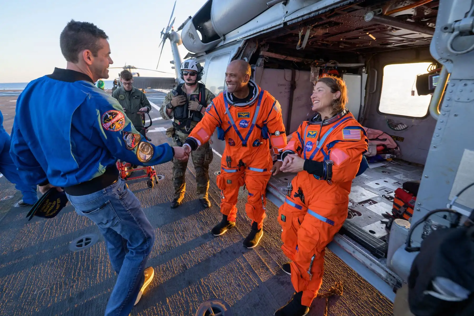 El astronauta de la NASA Victor Glover, piloto de Artemis II  y la astronauta de la NASA Christina Koch, especialista de la misión Artemis II, conversan con el administrador de la NASA, Jared Isaacman, en su helicóptero MH-60 Seahawk de la Armada, perteneciente al Escuadrón de Combate Marítimo de Helicópteros (HSC) 23, en la cubierta de vuelo del USS John P. Murtha, tras ser rescatados de su nave espacial Orion después del amerizaje. Crédito de la imagen: NASA/Bill Ingalls