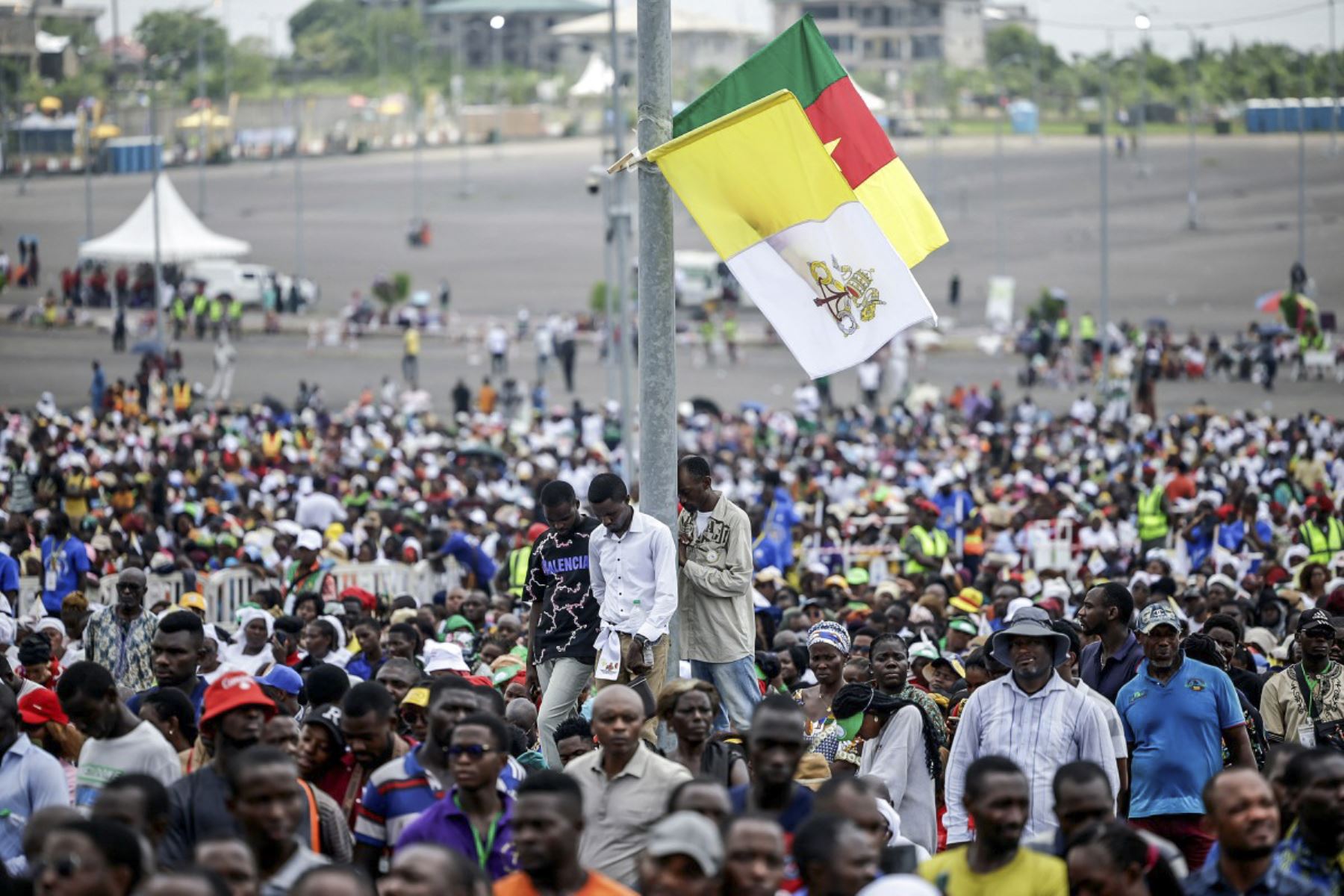 Los fieles rezan rodeando un poste con el Vaticano y las banderas de Camerún mientras el Papa León XIV dirige la Santa Misa en el área frente al Estadio Japoma en Douala el quinto día de un viaje apostólico de 11 días a África, el 17 de abril de 2026. (Foto de Patrick MEINHARDT / AFP)