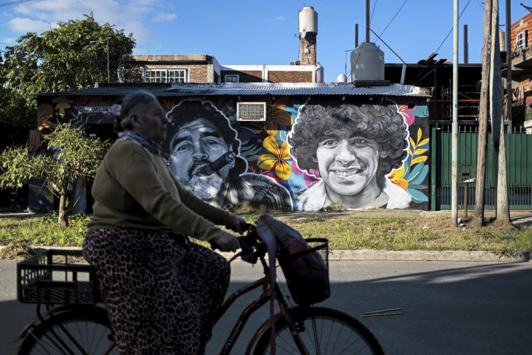 Una mujer pasa en bicicleta por murales que representan a la difunta estrella del fútbol Diego Maradona en el barrio de su ciudad natal, Villa Fiorito, en la provincia de Buenos Aires, Argentina. Foto: AFP