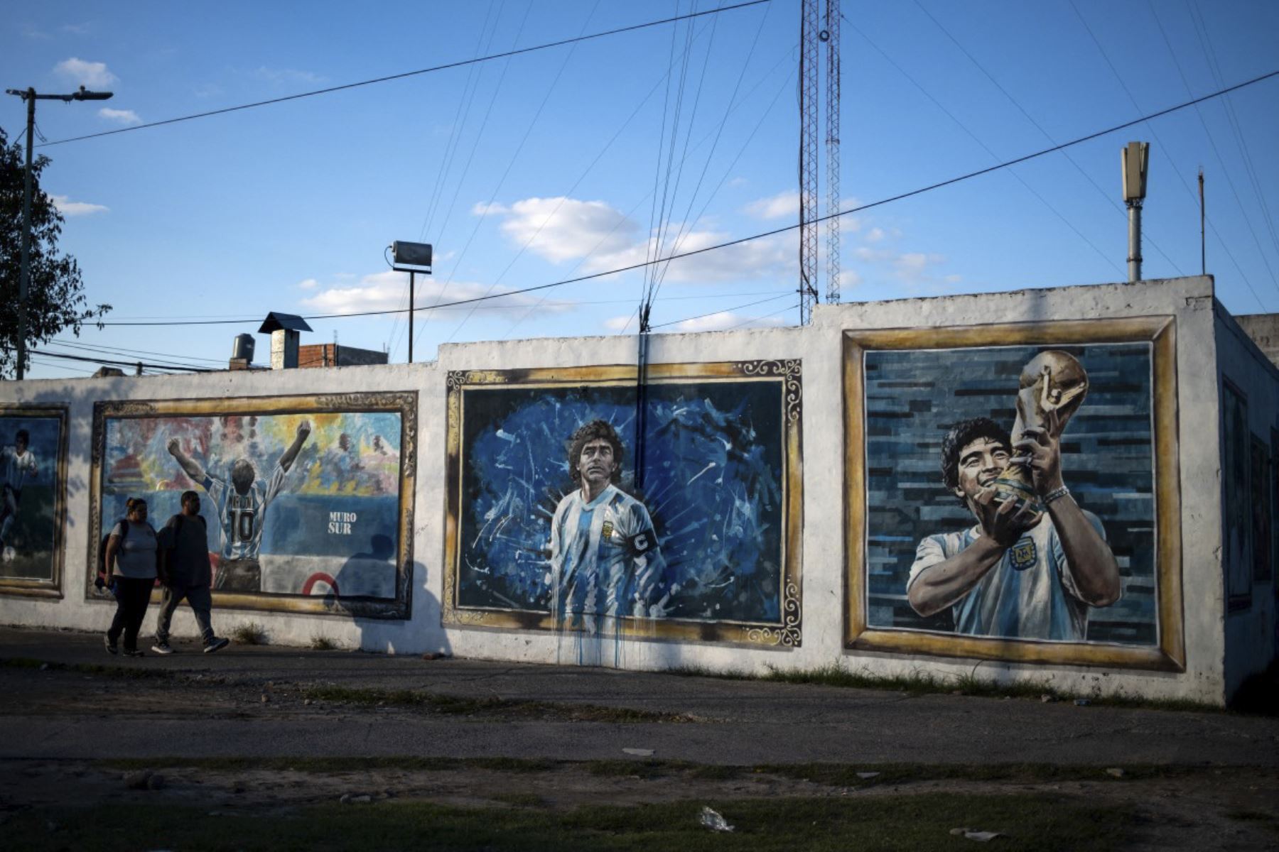 La gente pasa por los murales que representan a la difunta estrella del fútbol Diego Maradona en el barrio de su ciudad natal, Villa Fiorito, en la provincia de Buenos Aires, Argentina. Foto: AFP