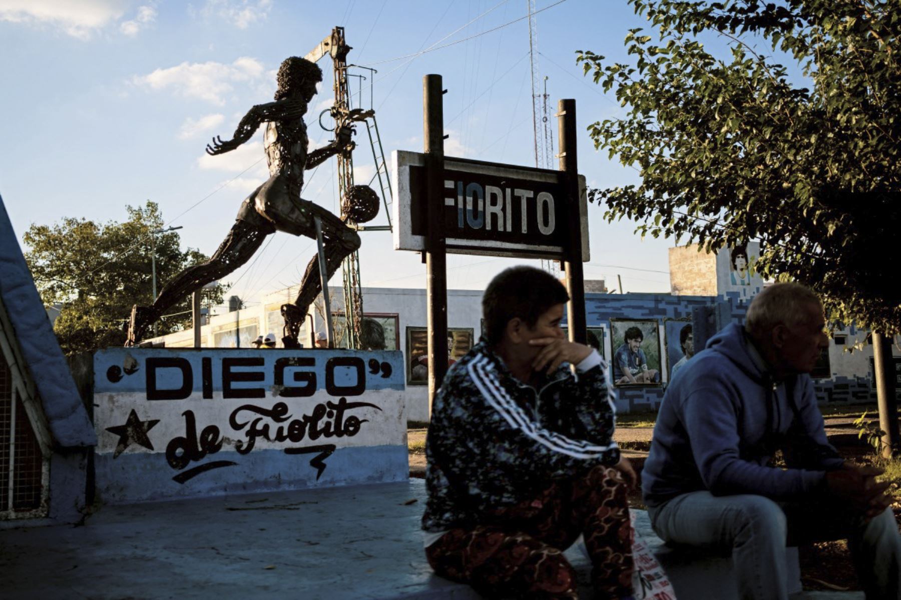 La gente se sienta junto a una estatua que representa a la difunta estrella del fútbol Diego Maradona en el barrio de su ciudad natal, Villa Fiorito, en la provincia de Buenos Aires, Argentina. Foto: AFP