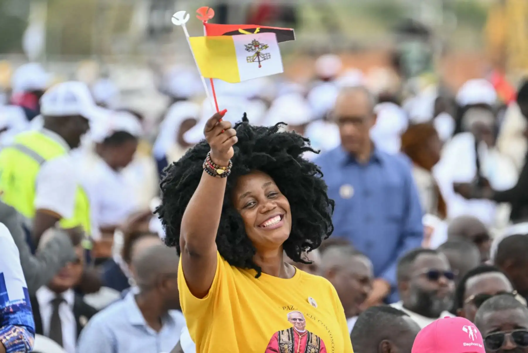 Un fiel portando banderas del Vaticano y de Angola aplaude a la llegada del Papa León XIV en el Papamóvil para oficiar una Santa Misa en Kilamba, en el séptimo día de un viaje apostólico de 11 días a África. Foto: ANDINA/AFP