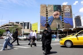 Una mujer camina cerca de una valla publicitaria que representa el estrecho de Ormuz con una leyenda en persa: "Siempre en manos de Irán". Teherán (mayo de 2026). Foto: AFP.
