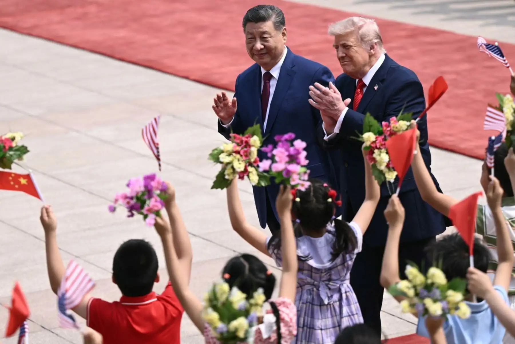 El presidente de Estados Unidos, Donald Trump, y el presidente de China, Xi Jinping, saludan a niños que ondean banderas nacionales chinas y estadounidenses y flores durante la ceremonia de bienvenida en el Gran Salón del Pueblo en Beijing el 14 de mayo de 2026. Foto: AFP
