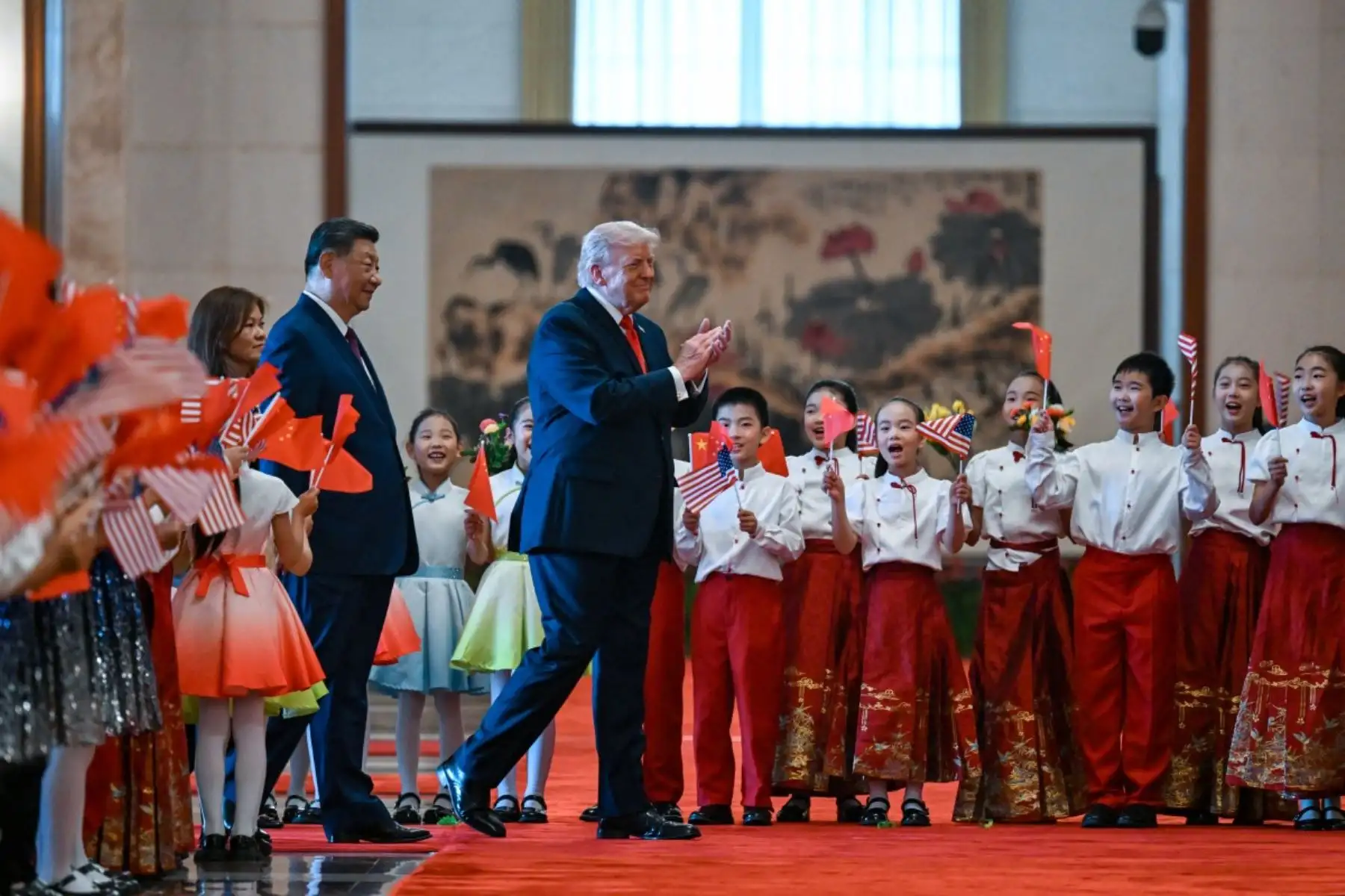 El presidente de Estados Unidos, Donald Trump, y el presidente de China, Xi Jinping, saludan a niños que ondean banderas nacionales chinas y estadounidenses y flores durante la ceremonia de bienvenida en el Gran Salón del Pueblo en Beijing el 14 de mayo de 2026. Foto: AFP
