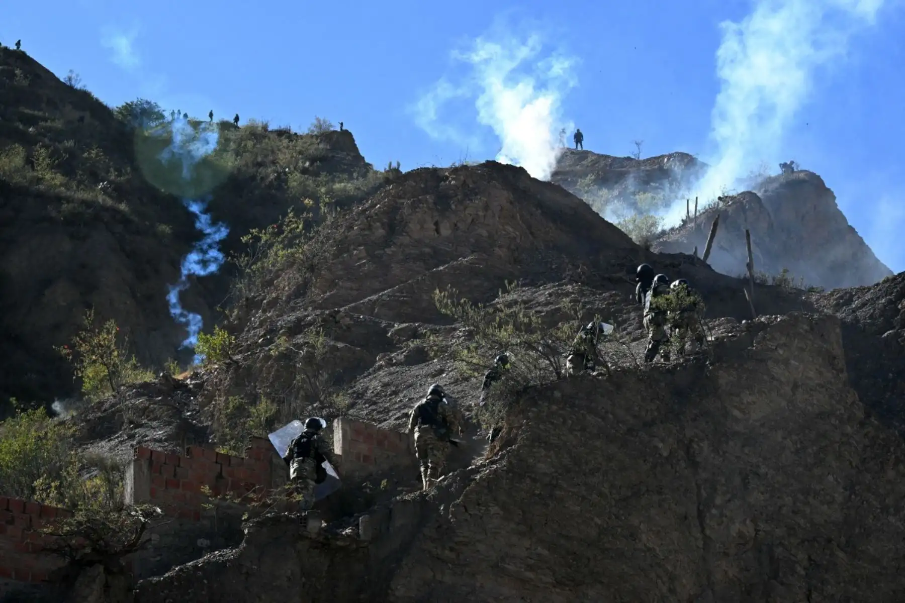 Los agentes de policía antidisturbios avanzan a lo largo de una ladera en medio de gases lacrimógenos durante los enfrentamientos con manifestantes rurales en Lipari, departamento de La Paz, Bolivia, el 16 de mayo de 2026. El gobierno de Bolivia llegó a un acuerdo el 15 de mayo con miles de mineros que se enfrentaron a la policía en una protesta que paralizó el centro de La Paz. Sin embargo, otros sectores continúan bloqueando las rutas de acceso a la ciudad, hogar del poder ejecutivo y el Congreso. (Foto d
