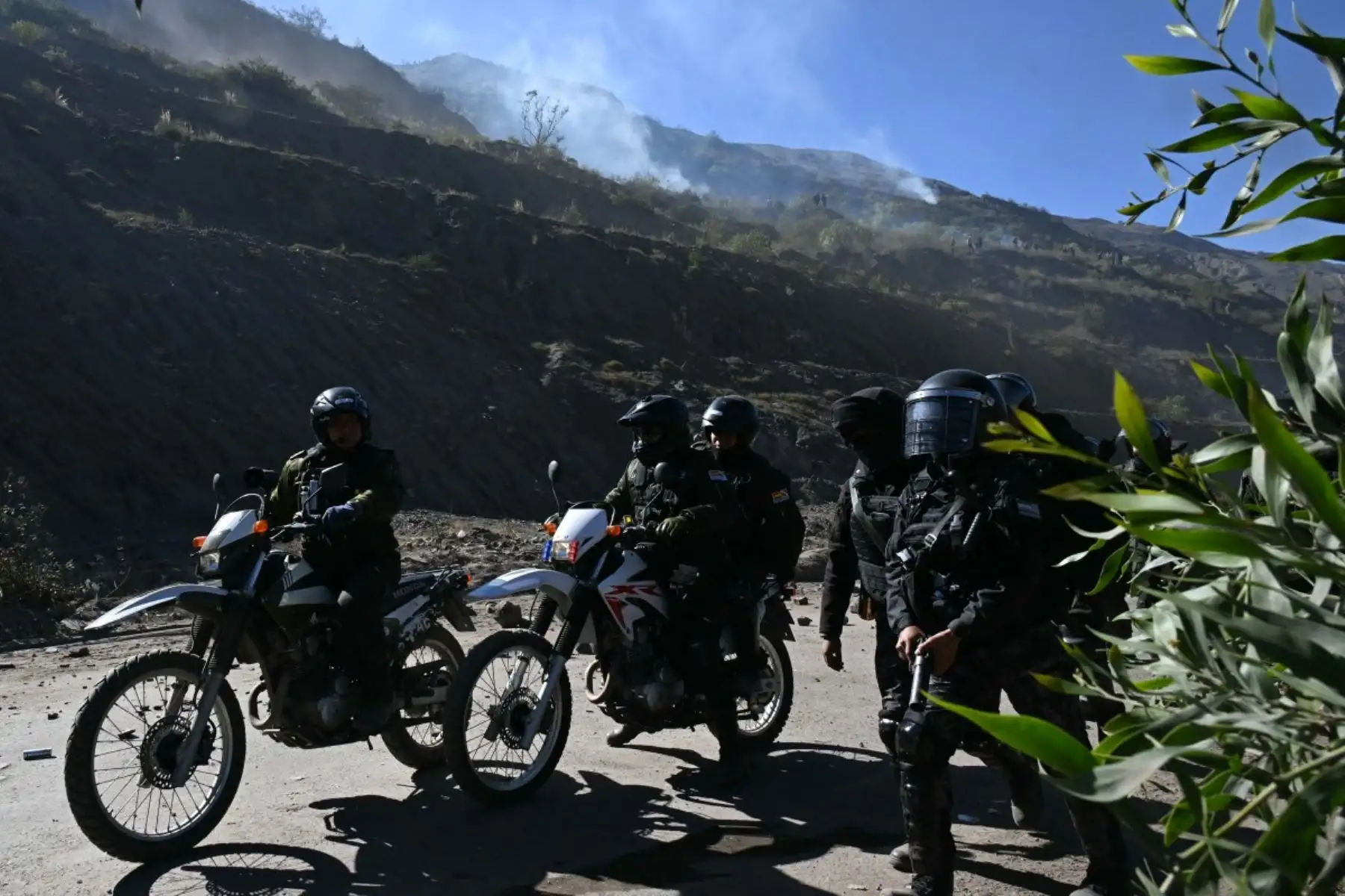 Los agentes de policía antidisturbios conducen motocicletas a lo largo de una carretera mientras el gas lacrimógeno se desplaza sobre una ladera durante los enfrentamientos con manifestantes rurales en Lipari, departamento de La Paz, Bolivia, el 16 de mayo de 2026. El gobierno de Bolivia llegó a un acuerdo el 15 de mayo con miles de mineros que se enfrentaron a la policía en una protesta que paralizó el centro de La Paz. Sin embargo, otros sectores continúan bloqueando las rutas de acceso a la ciudad, hogar
