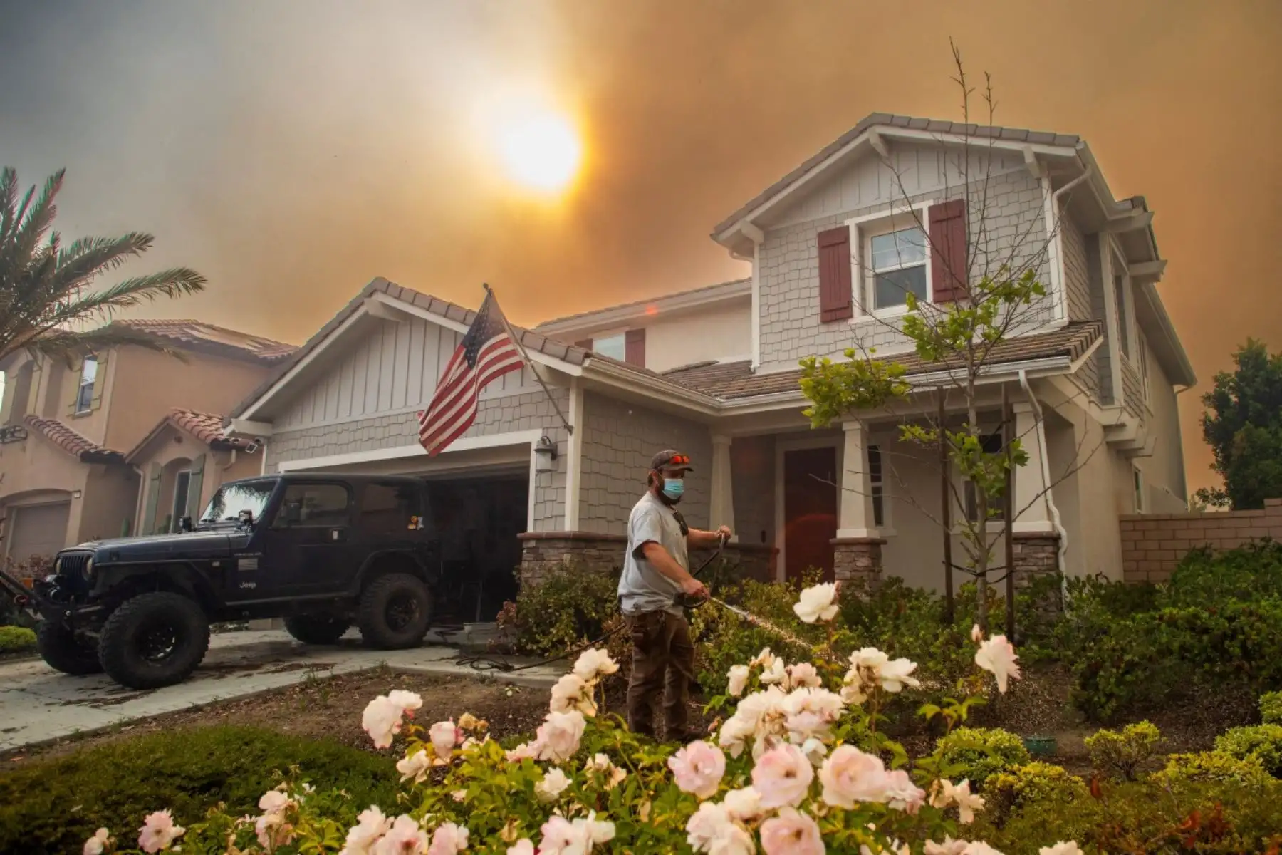 Un residente riega las plantas de su jardín delantero con una manguera mientras el incendio Sandy arde en las colinas cercanas a una zona residencial en Simi Valley, California. Foto: AFP
