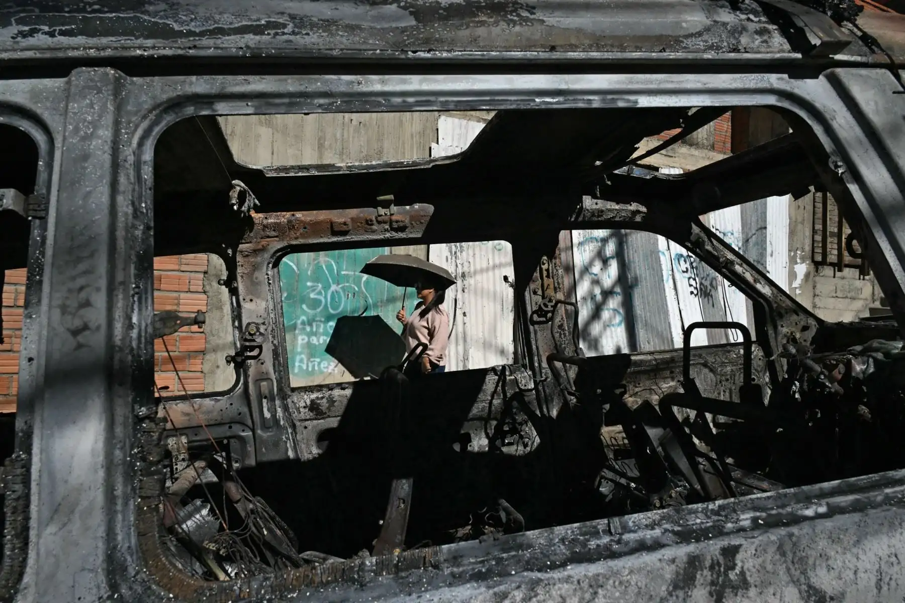 Una mujer pasa junto a un coche de policía quemado en La Paz, el 19 de mayo de 2026, el día después de una protesta exigiendo la renuncia del presidente de Bolivia, Rodrigo Paz. Foto: AFP